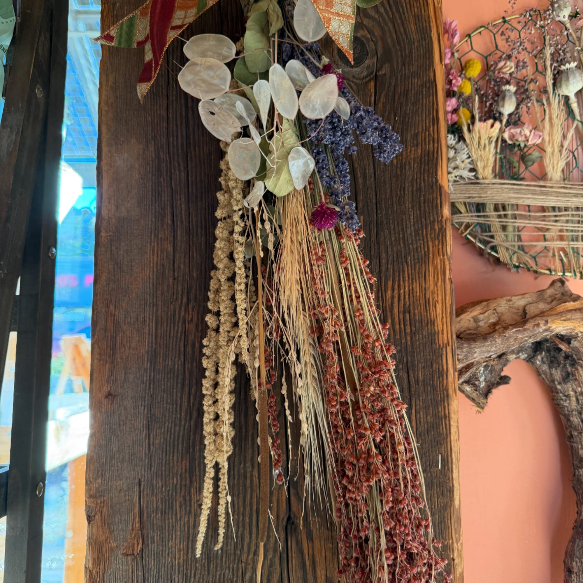 Dried floral hanging arrangement with pale seed pods and trailing grasses on wood