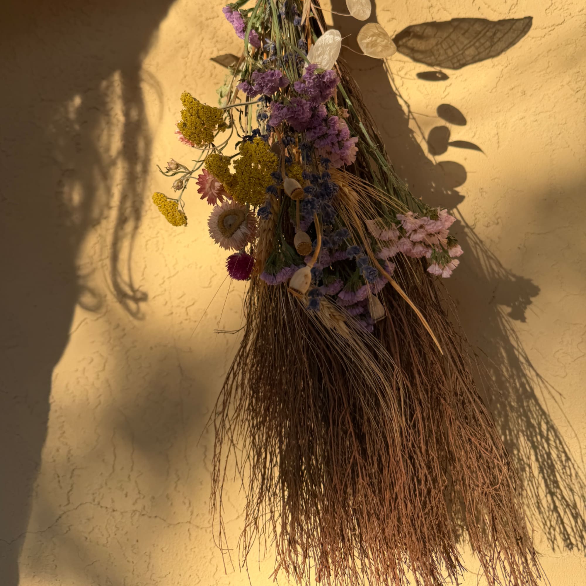 Dried floral hanging arrangement with purple and yellow blooms against a wall