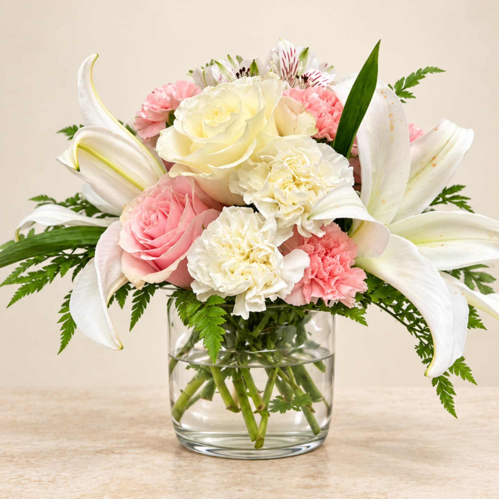Pink and white bouquet of roses, lilies, and carnations in a glass vase