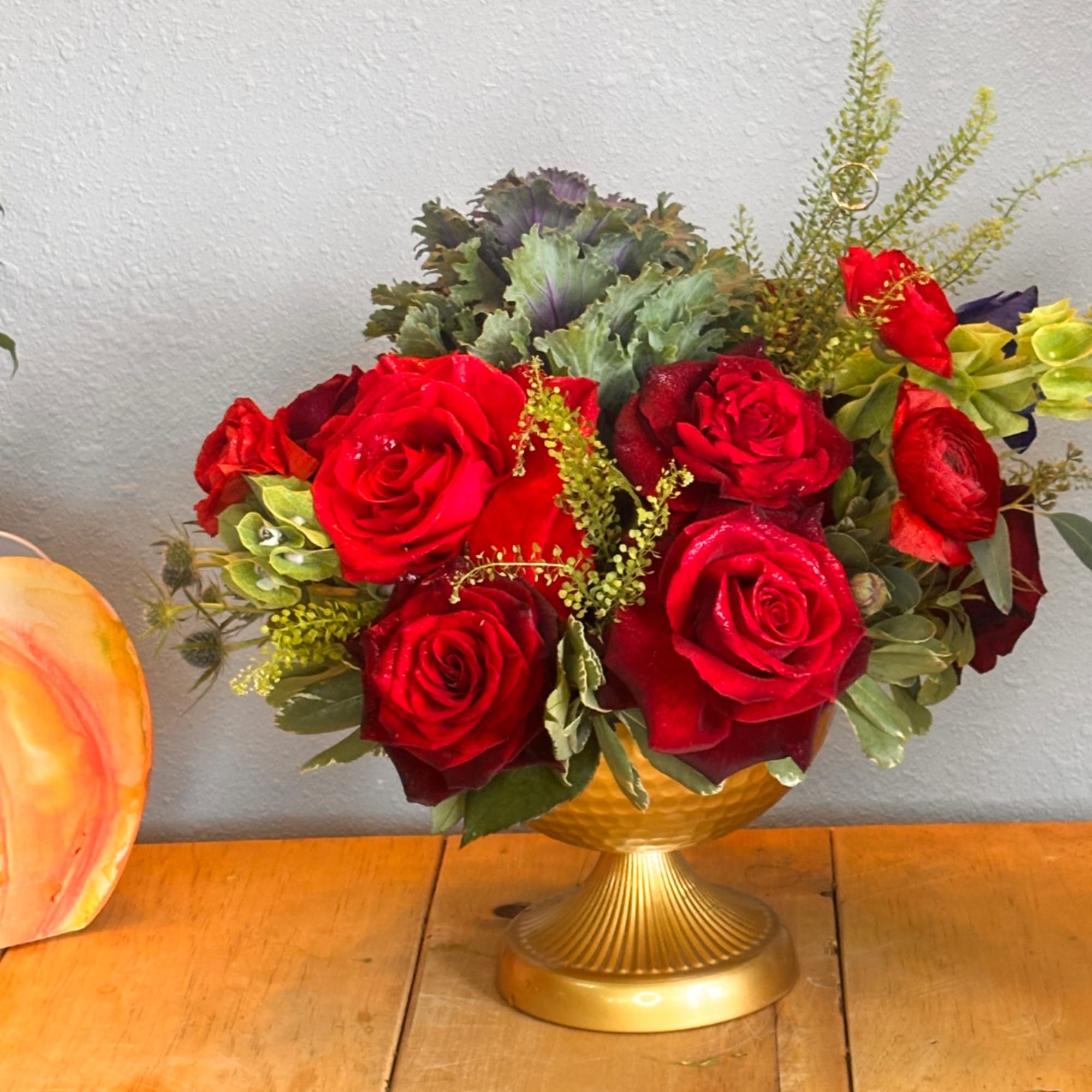 Red roses arranged in a gold pedestal vase with green foliage