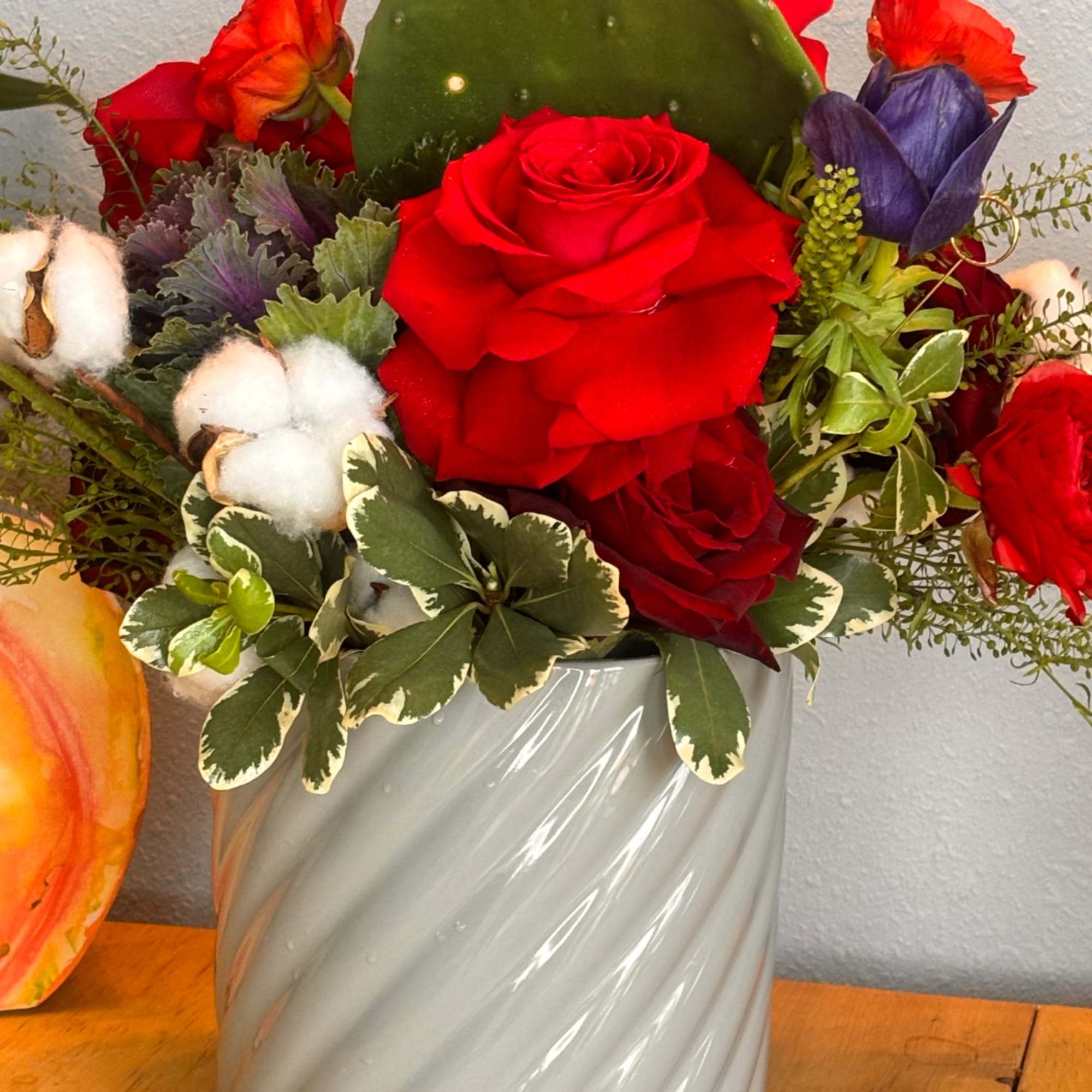 Red roses and mixed blooms in a white vase with cotton accents