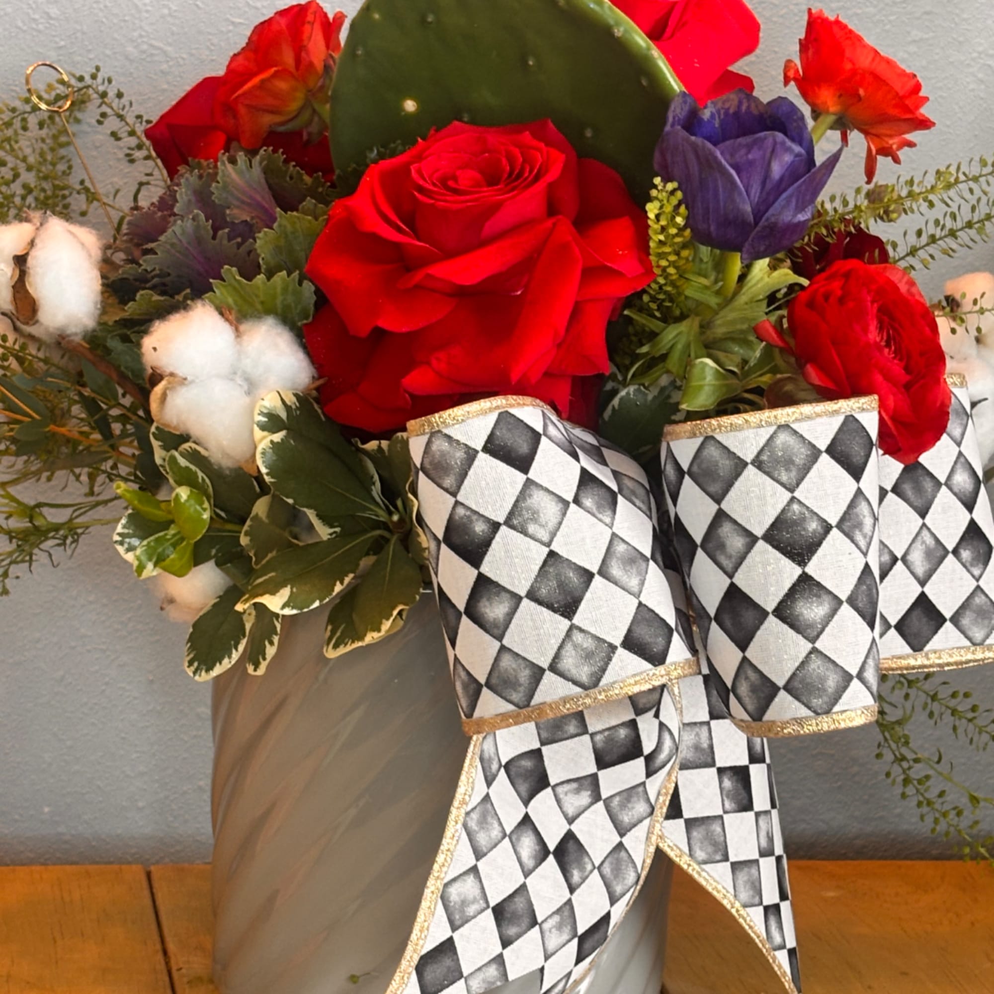Red roses and mixed flowers in a gray vase with a black-and-white ribbon
