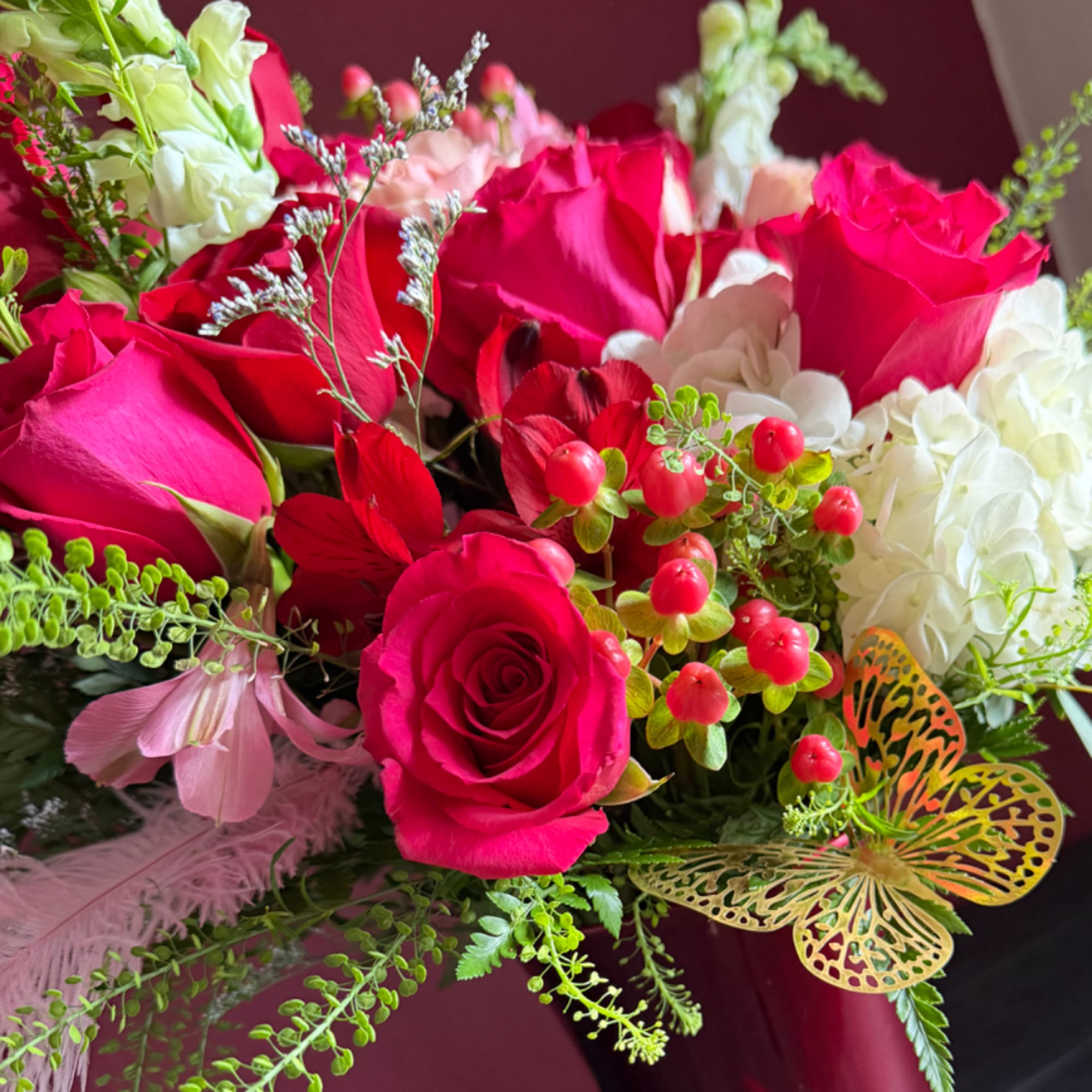 Bouquet of hot pink roses, white blooms, and red berries with butterfly accents