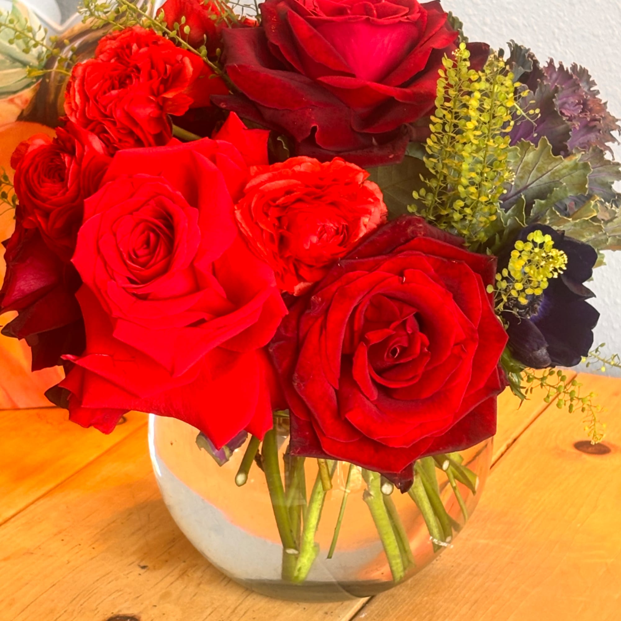 Red roses arranged in a clear glass vase with small yellow filler flowers