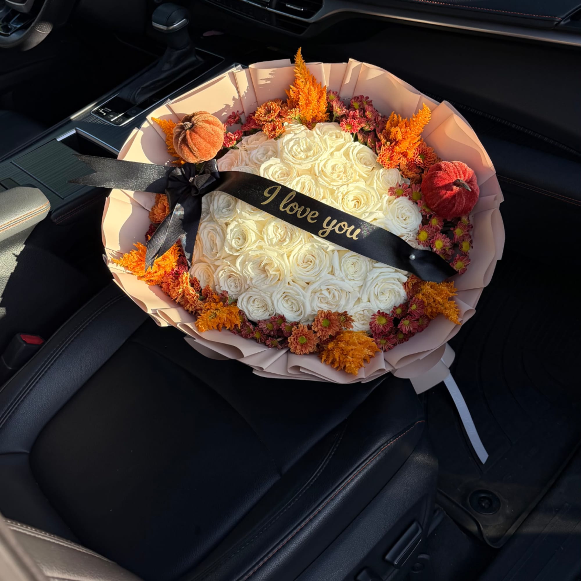 Bouquet of white roses with orange flowers and a black ribbon in a car seat