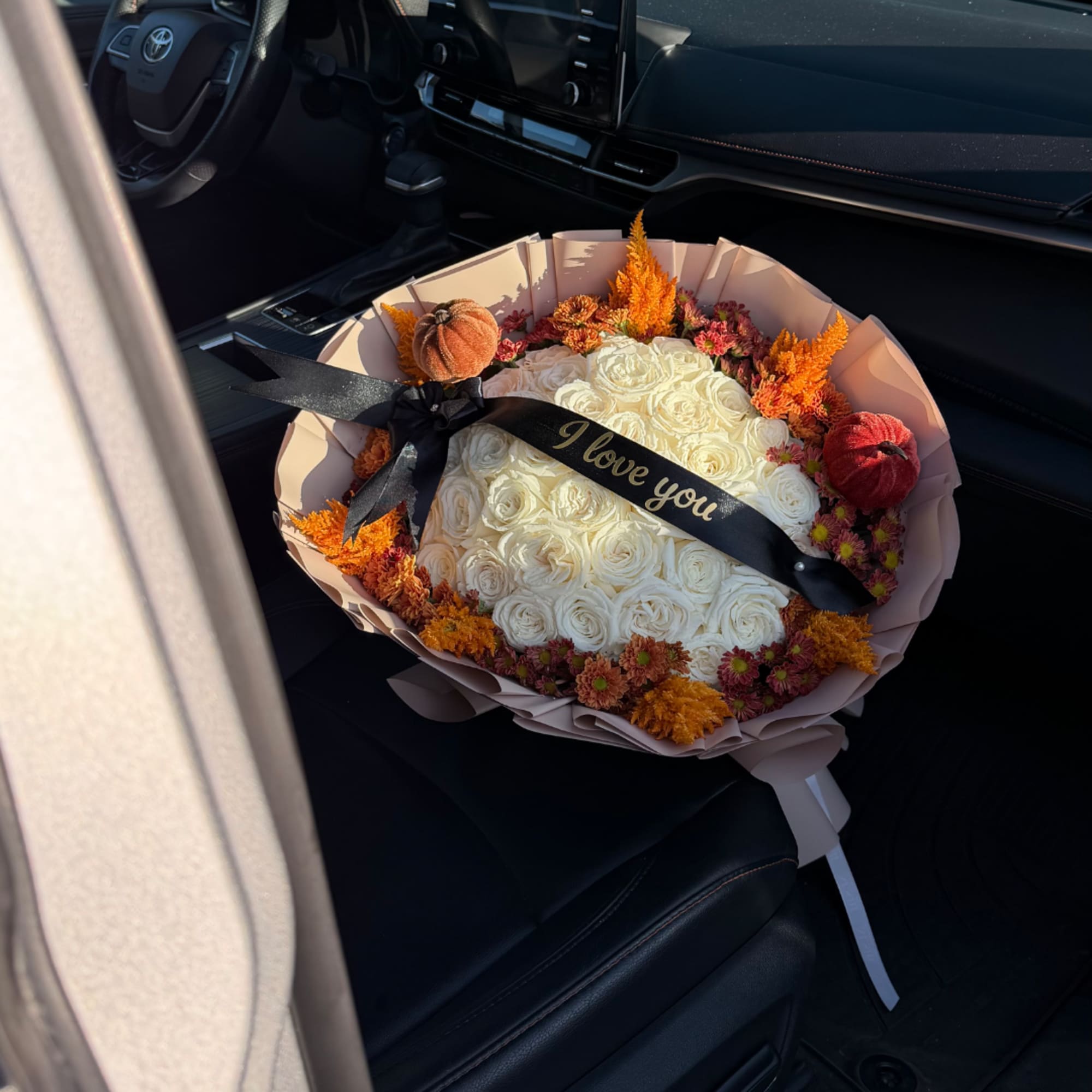 Bouquet of white roses with orange flowers and a black ribbon in a car seat