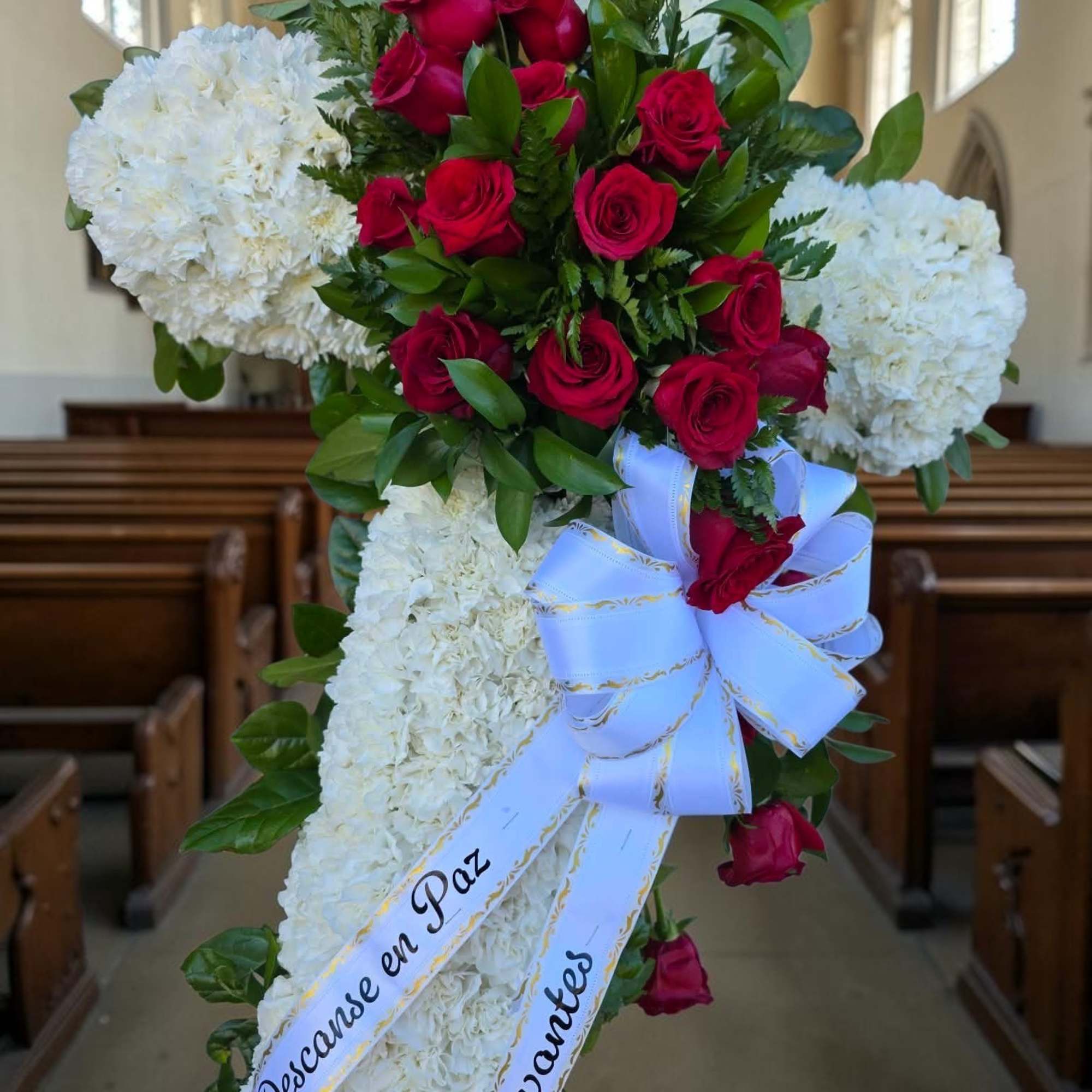 Red roses and white carnations arranged in a church setting with a white ribbon