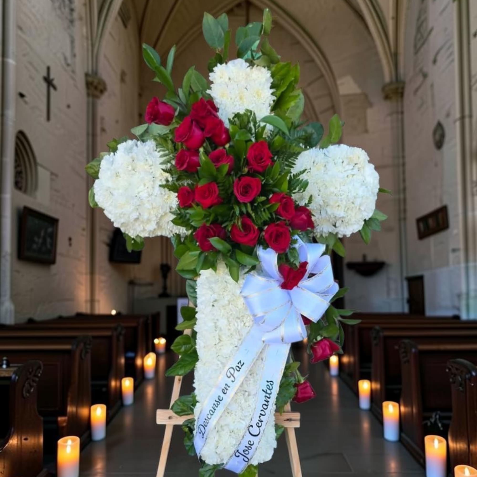 Cross-shaped floral tribute with red roses and white blooms on an easel