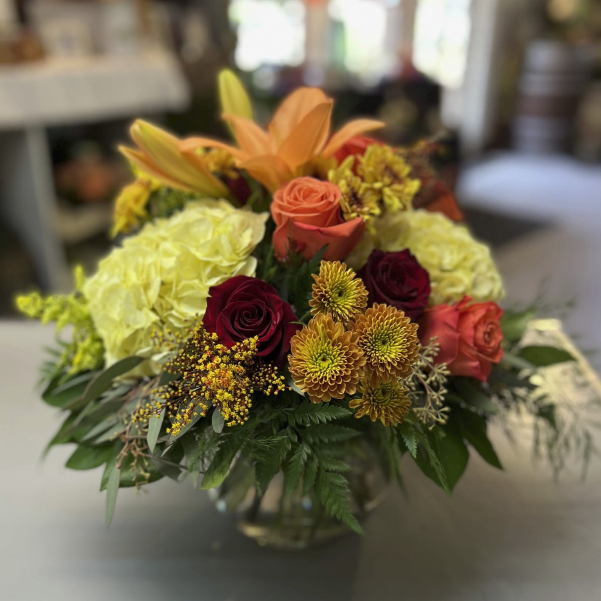 Mixed bouquet of roses, lilies, and mums in a glass vase