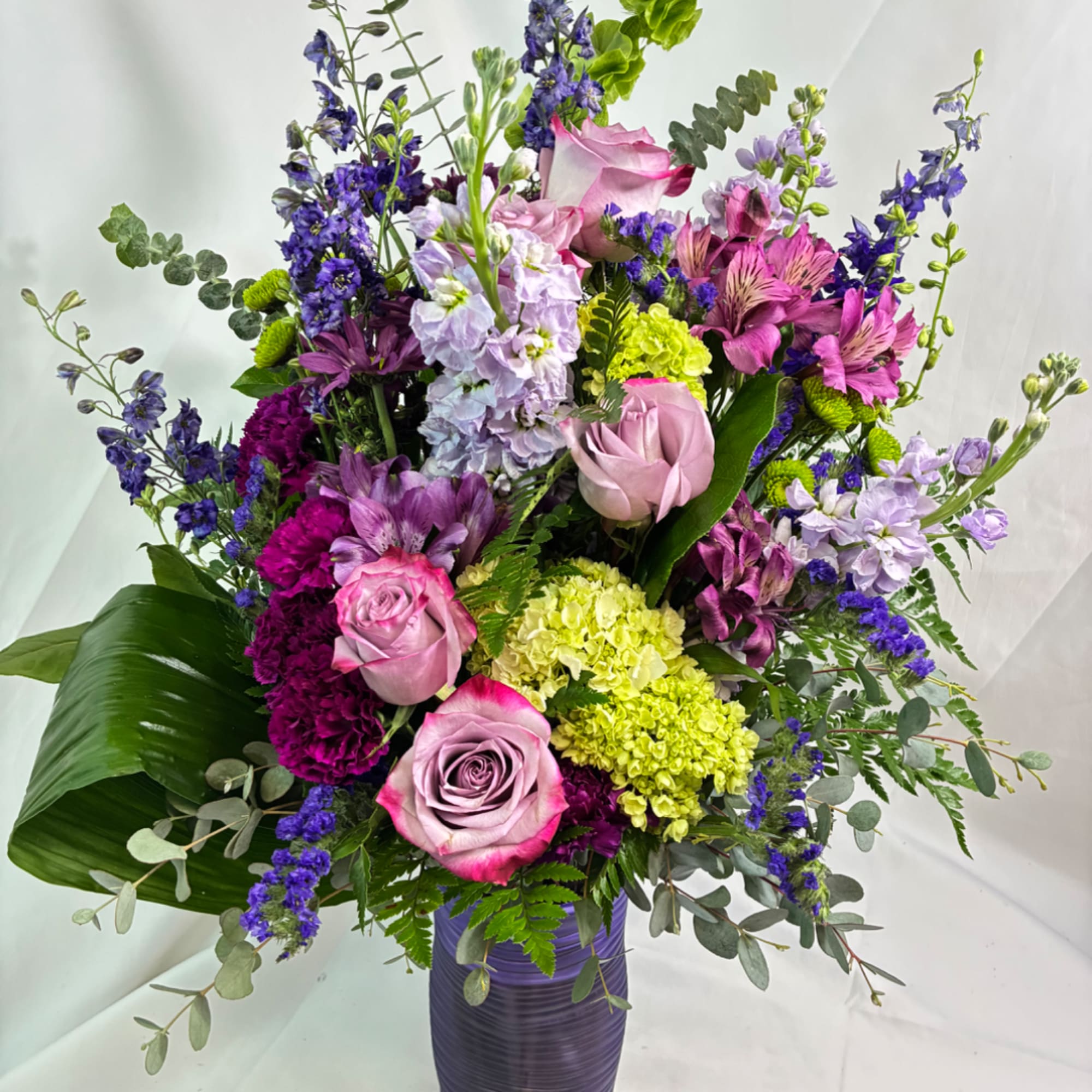 Tall mixed bouquet in a purple vase with pink roses and purple blooms