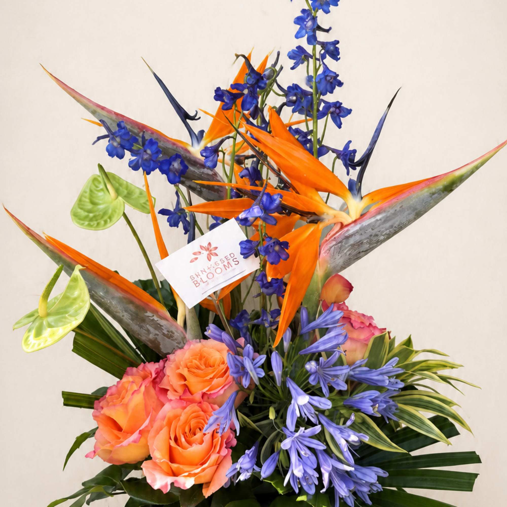 Tropical arrangement with orange birds of paradise and blue flowers in a low container