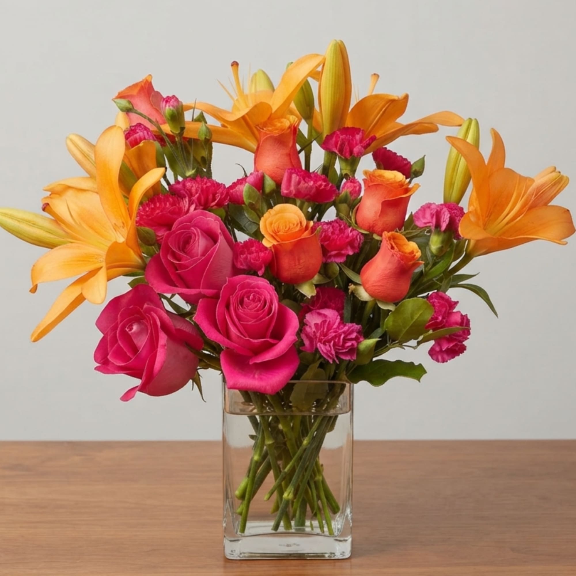 Pink roses and orange lilies arranged in a clear glass vase