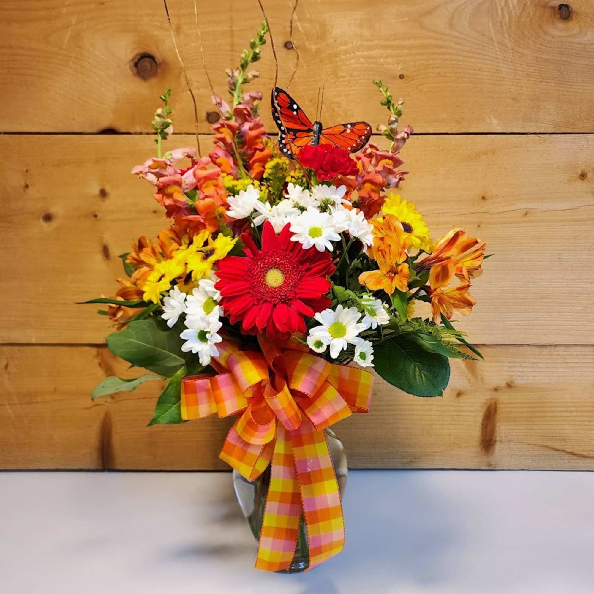 Mixed bouquet in a glass vase with a plaid ribbon and butterfly pick