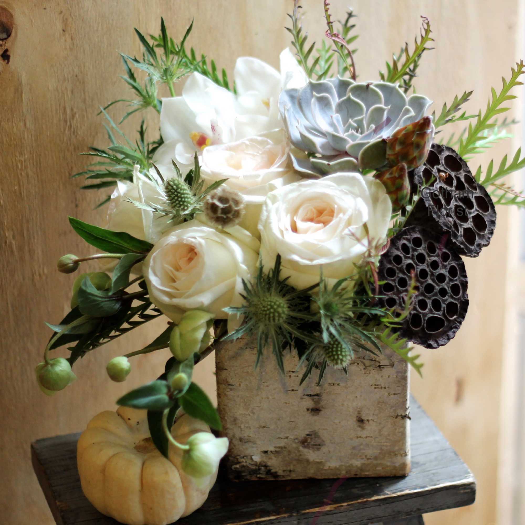 White roses and succulents in a rustic square container with a small pumpkin