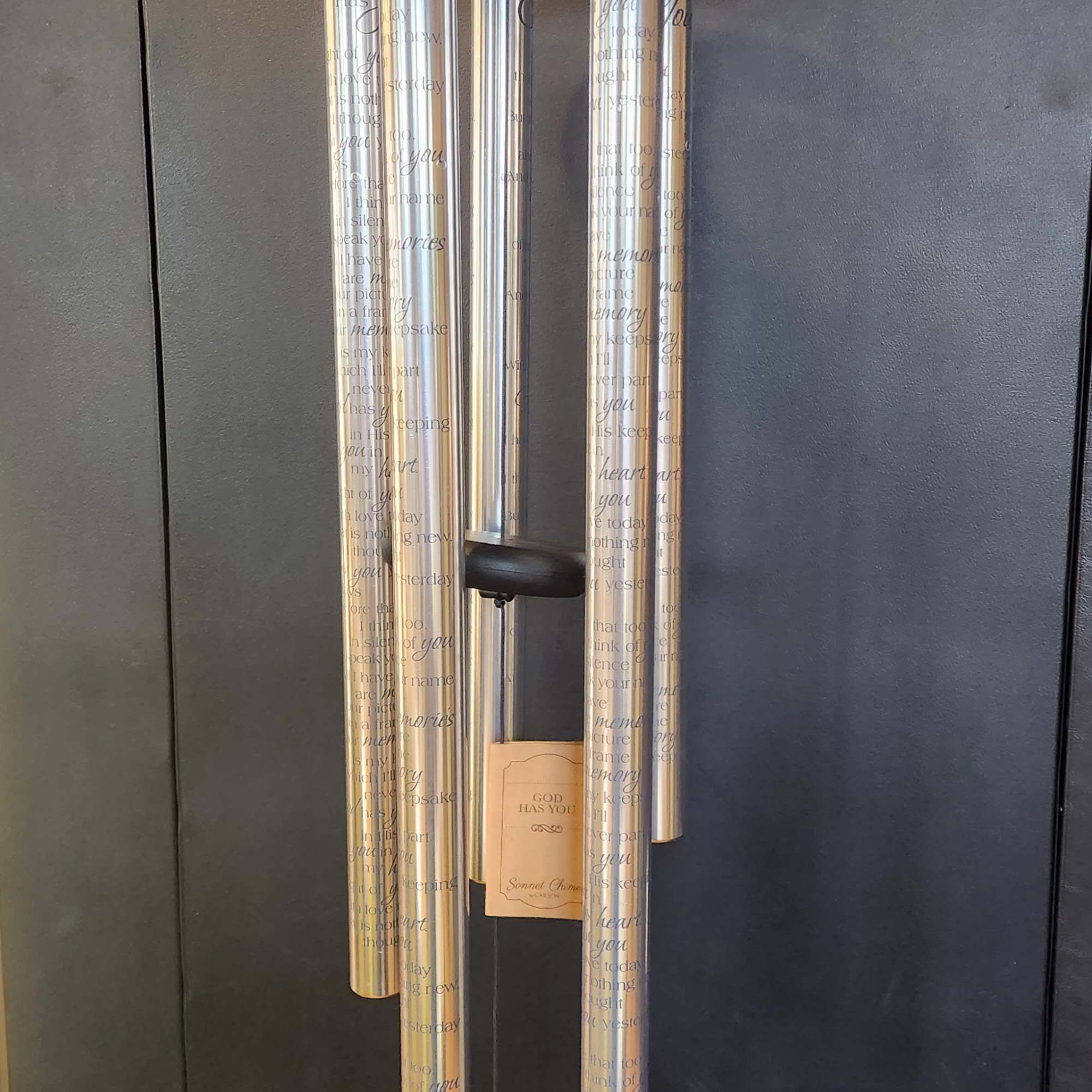 Silver memorial wind chime hanging against a dark wall
