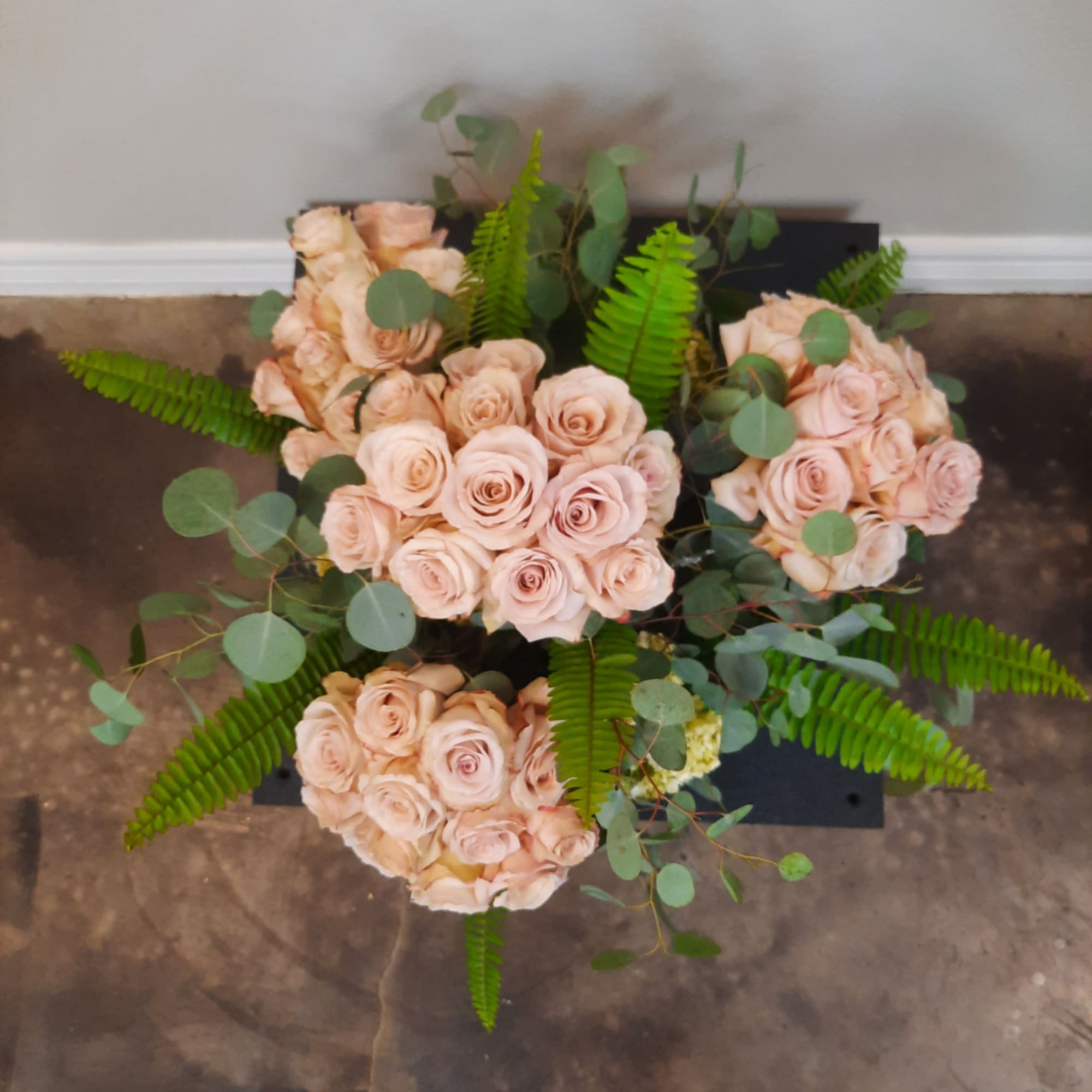 Three pale peach rose bouquets with fern and eucalyptus on a black base