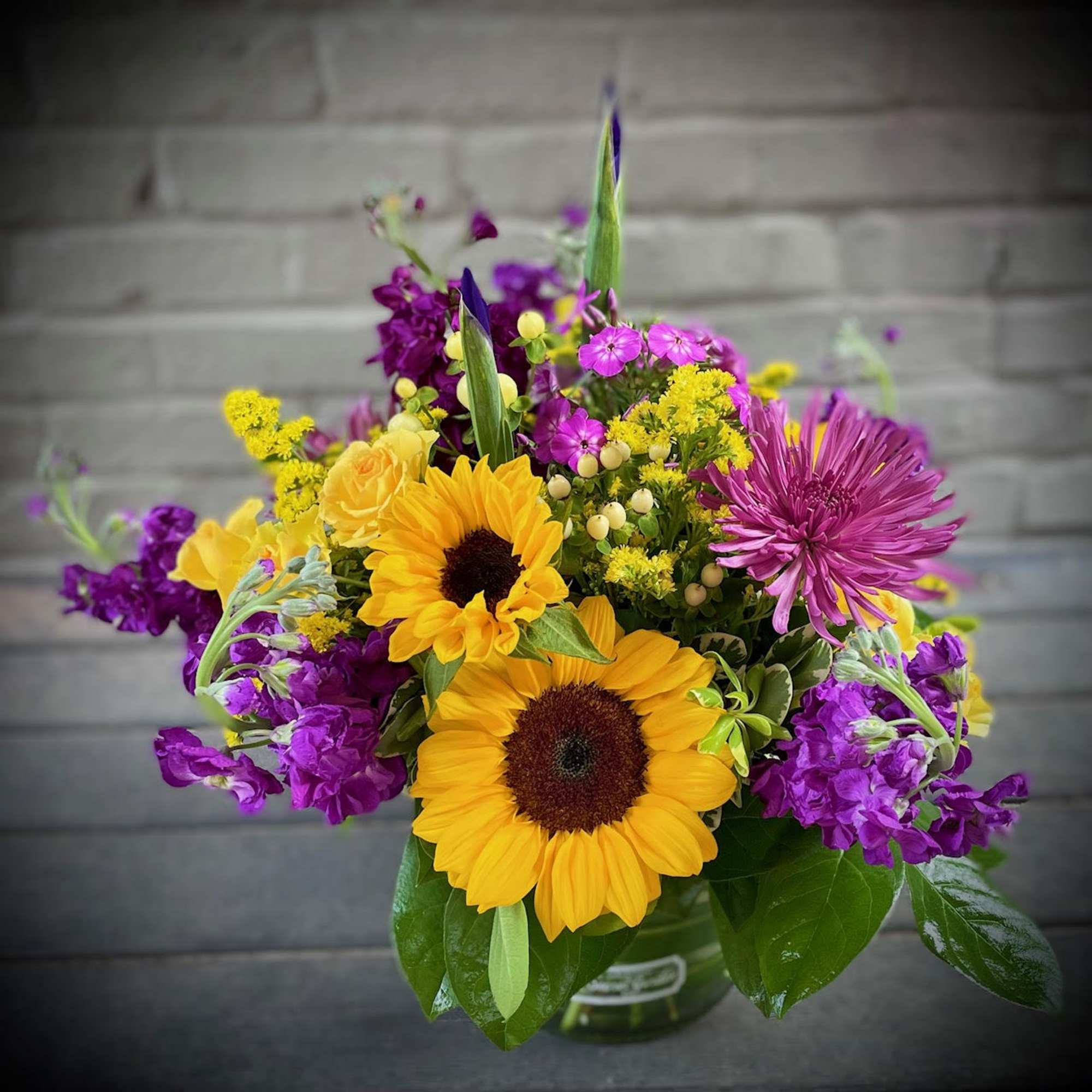 Full of yellow and purple hues, the Cheerful Glow features sunflowers, locally