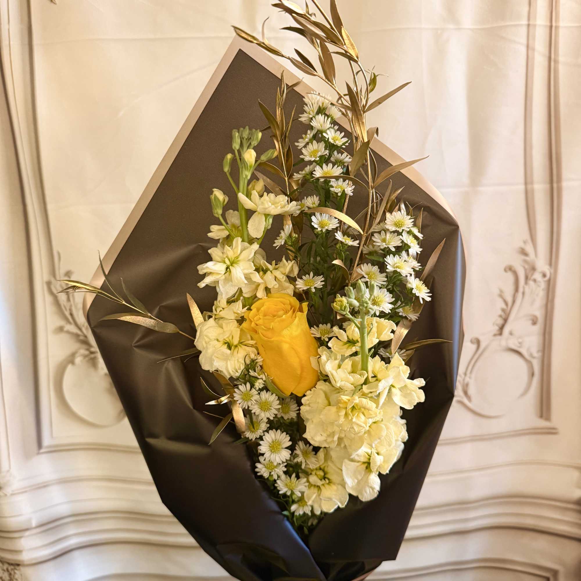 Bouquet of yellow and white flowers wrapped in black paper with a yellow ribbon