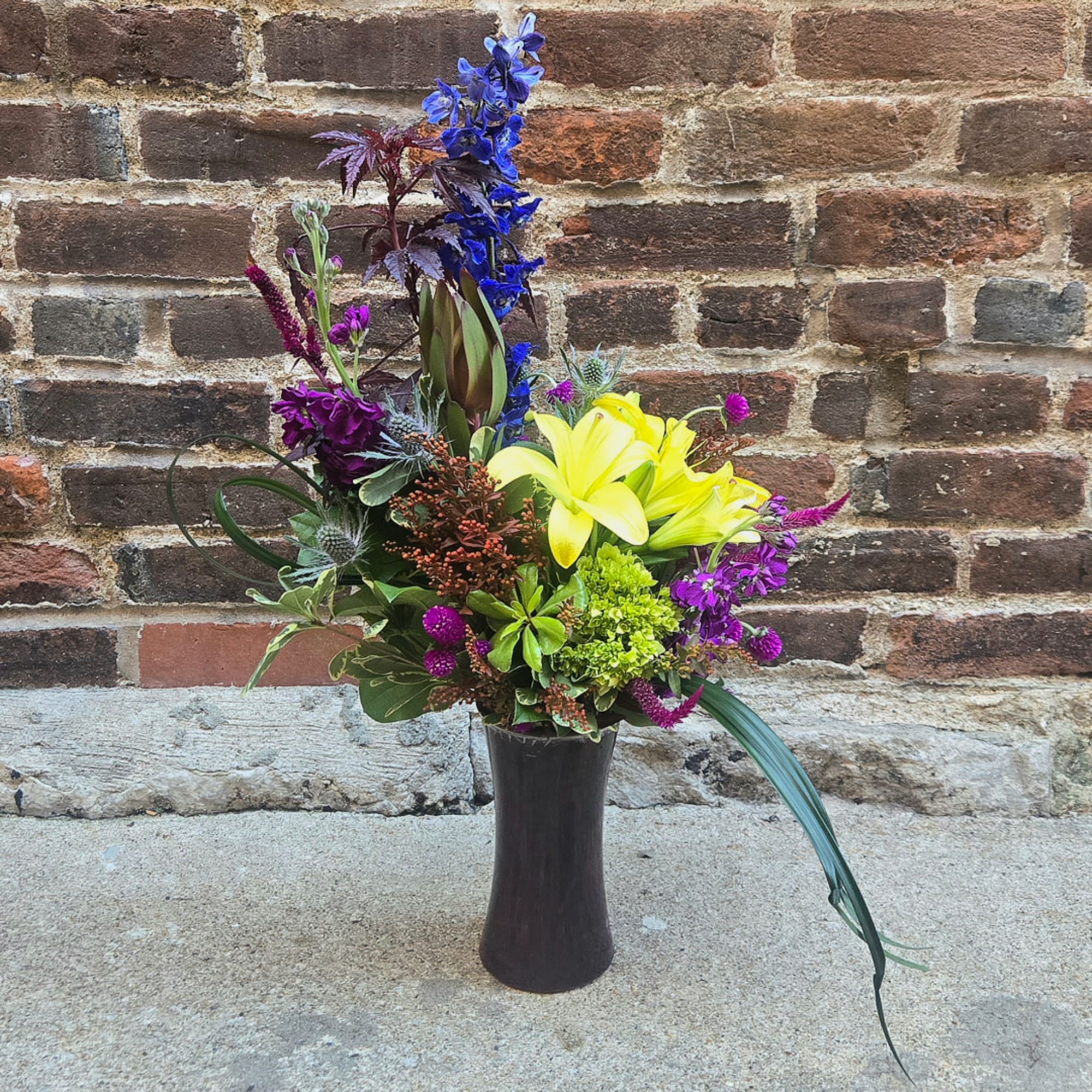 Tall mixed bouquet in a dark vase with yellow lilies and purple flowers