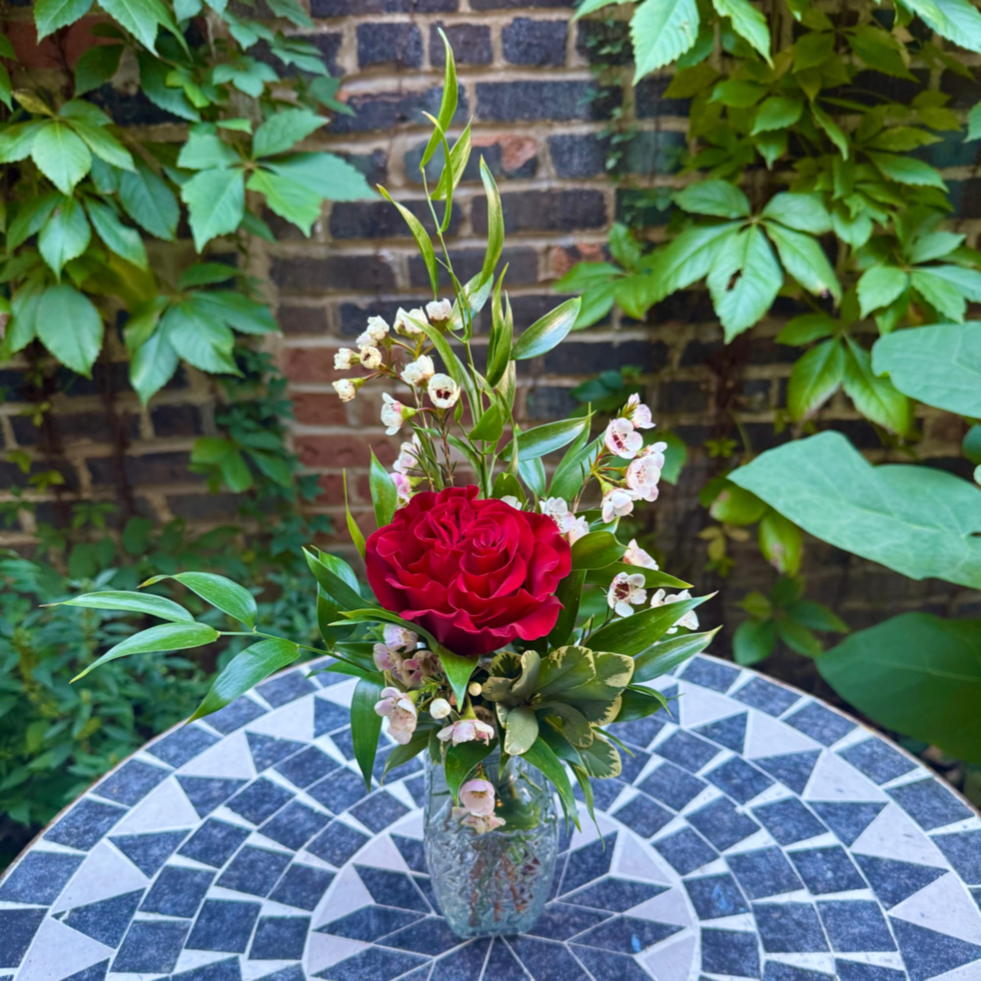 Red rose arrangement in a clear glass vase with small white blossoms