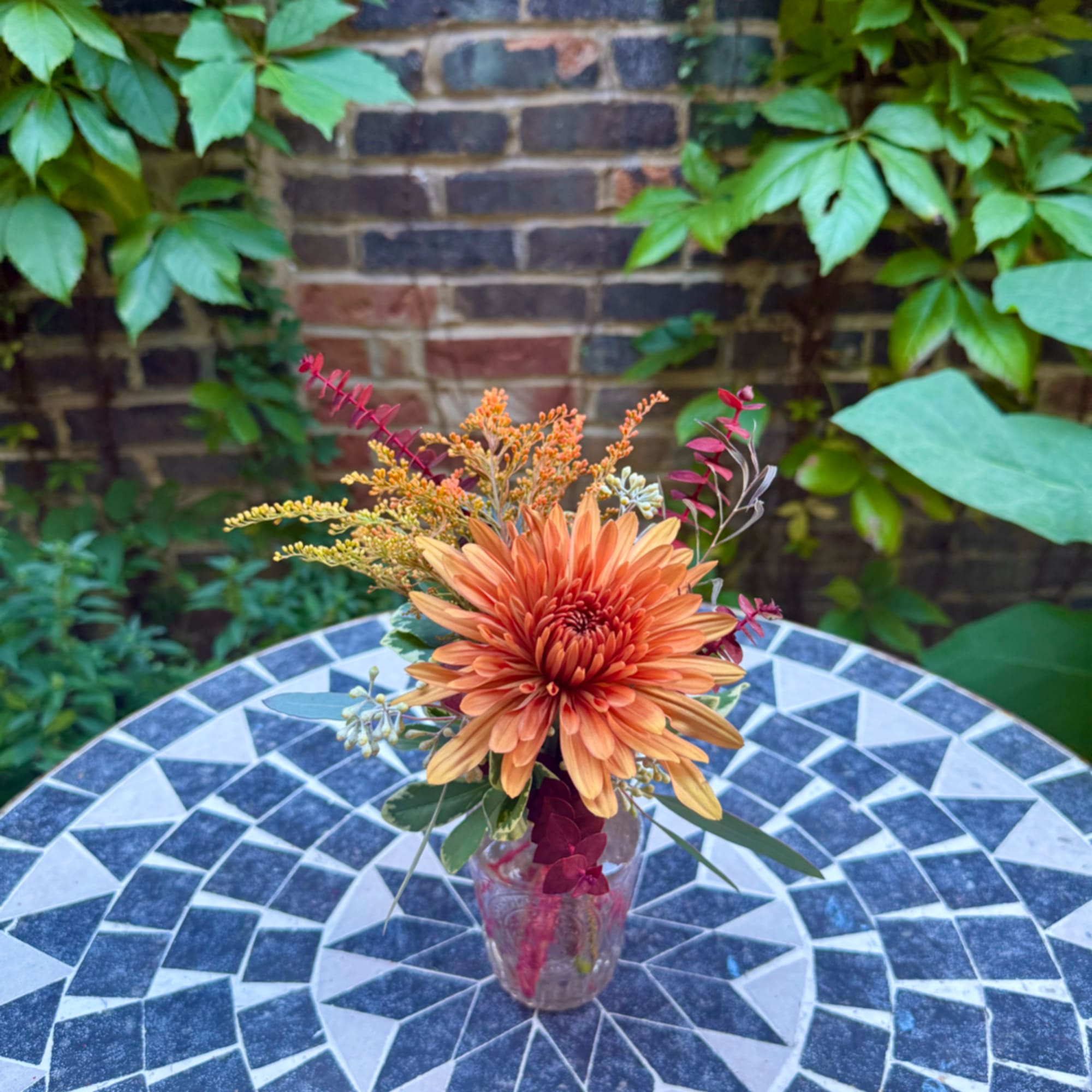 Orange chrysanthemum arrangement in a clear glass vase on a mosaic table