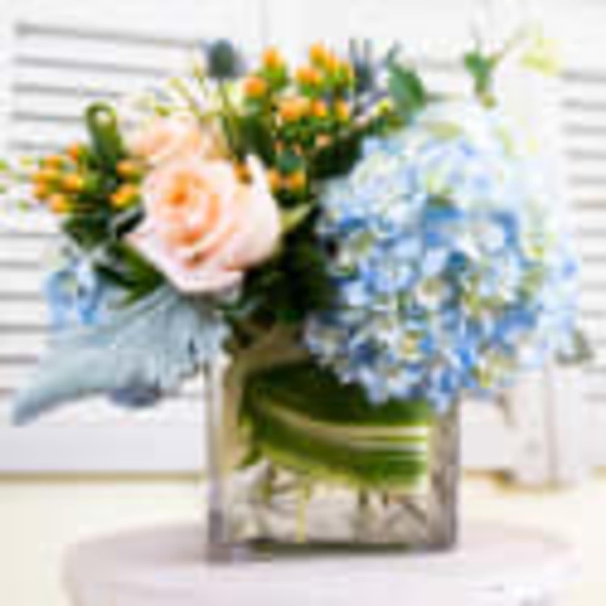 A cute cute vase with bue hydrangeas and peach roses and berries