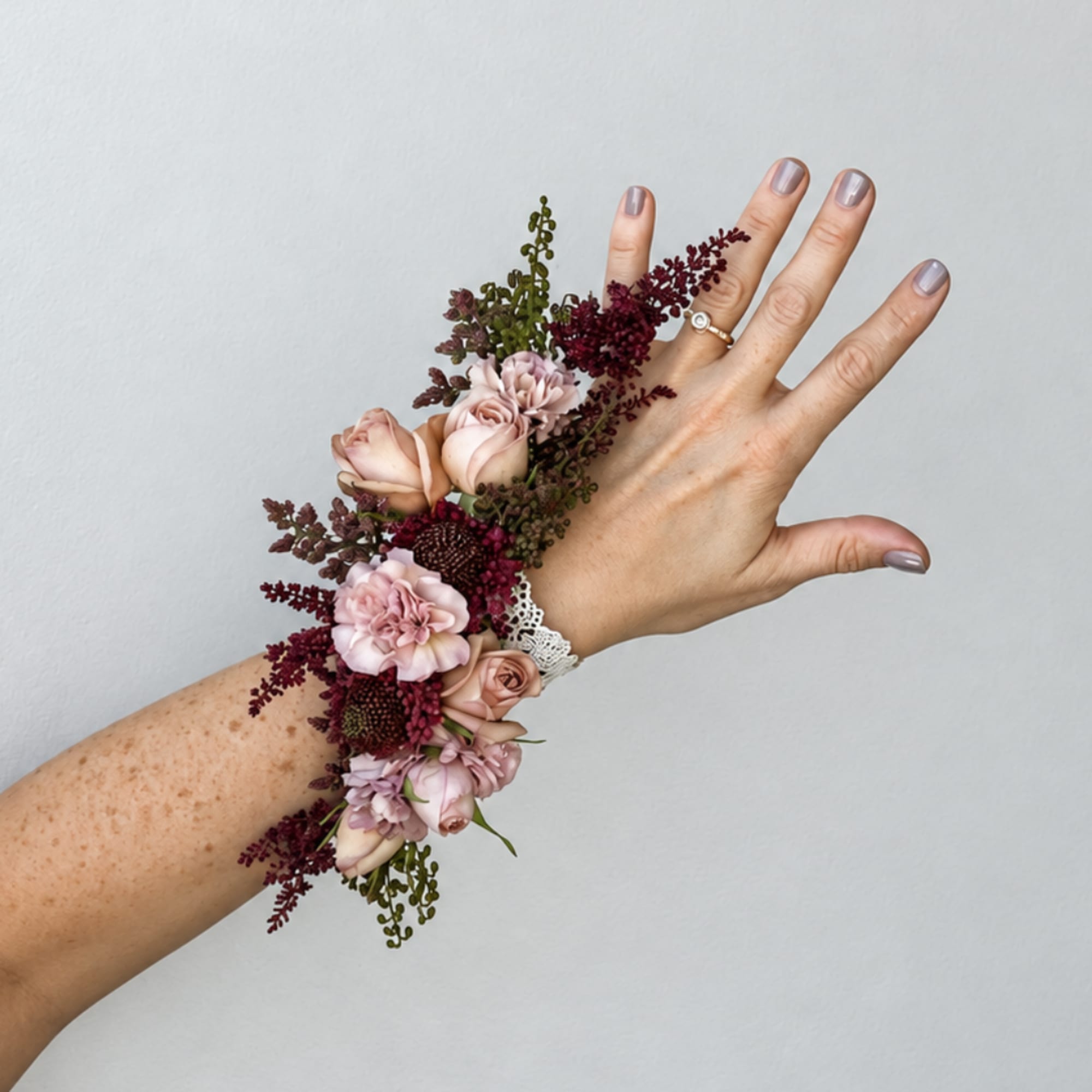 Floral wrist corsage with pale pink roses and burgundy accents on a hand
