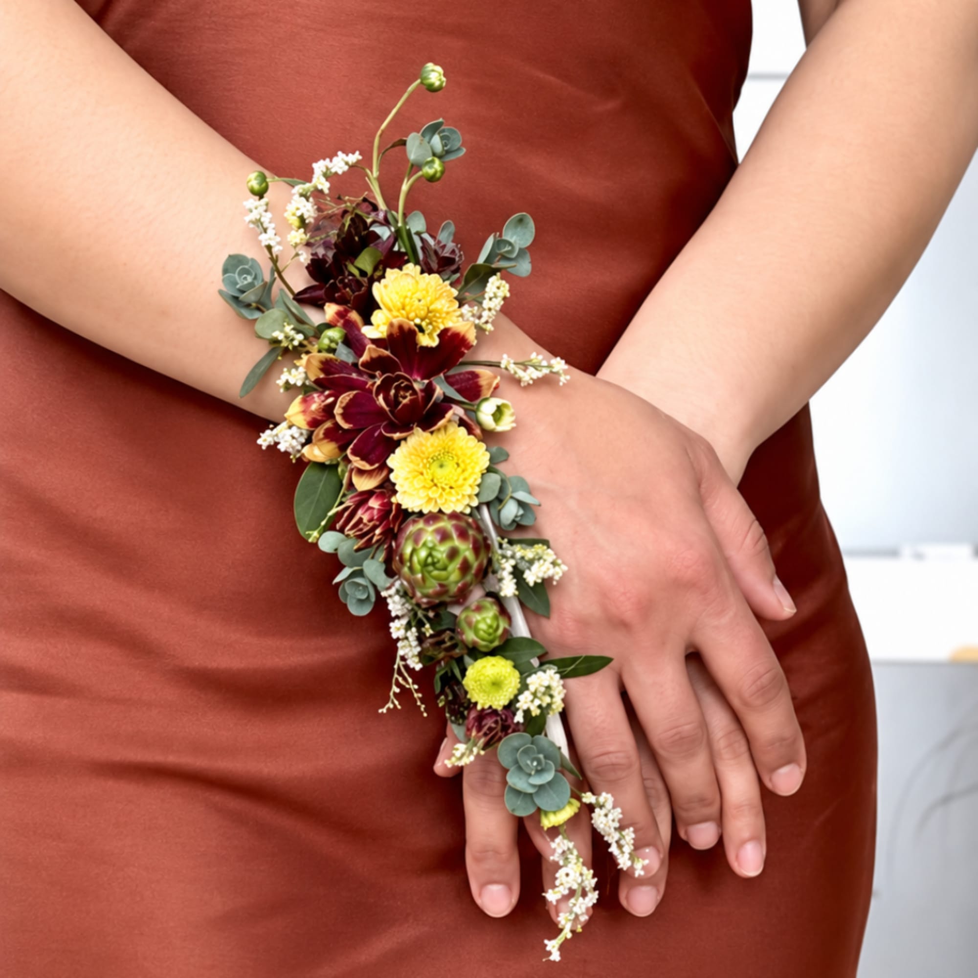 Floral wrist corsage with burgundy and yellow blooms on a person's hand