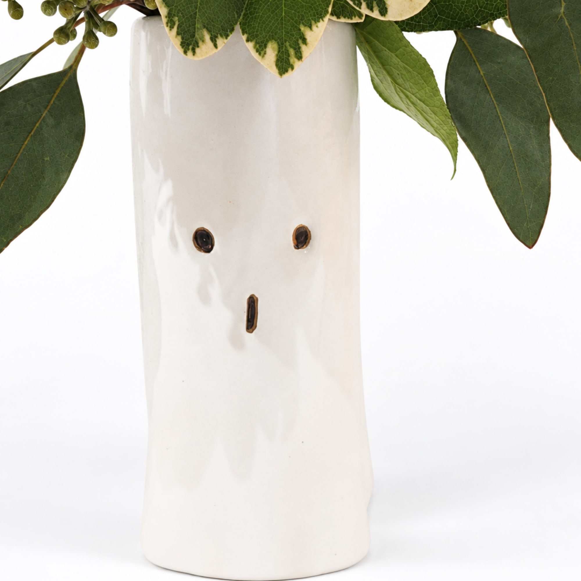 White ceramic vase with a face design and greenery at the top