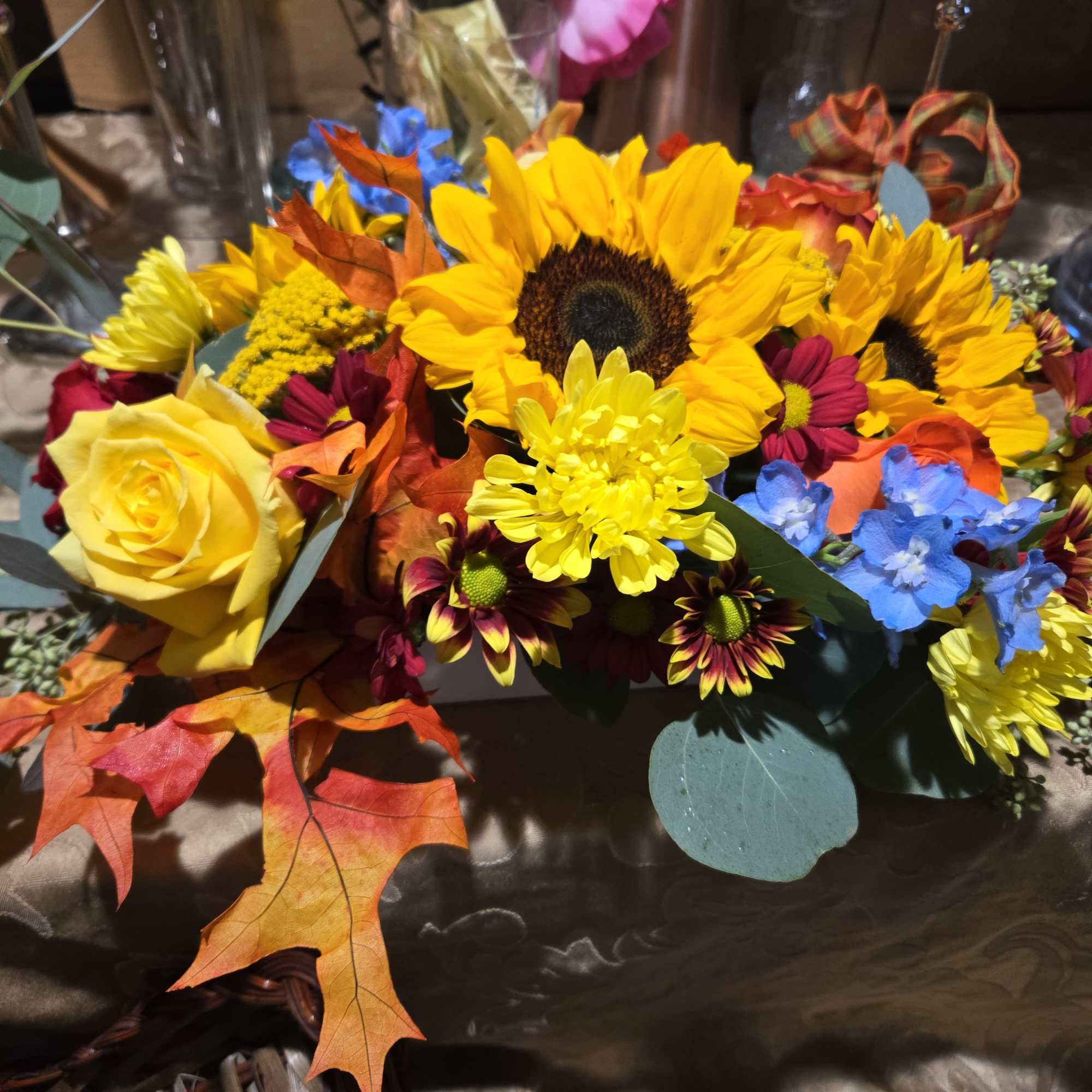 Beautiful assortment of fall colors, roses, mums, sunflowers. blue delphinium and preserve