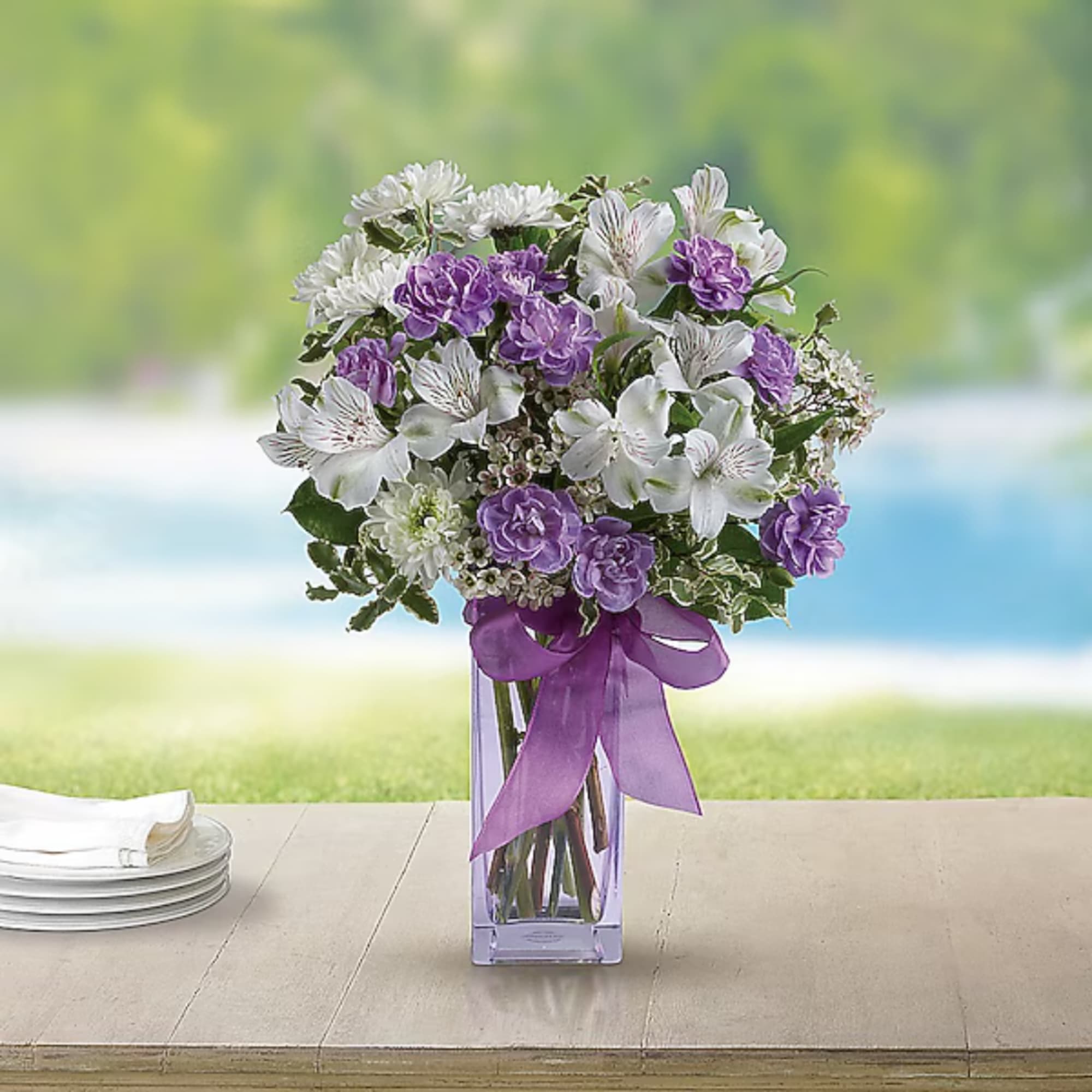 Purple and white bouquet in a clear square vase with a ribbon