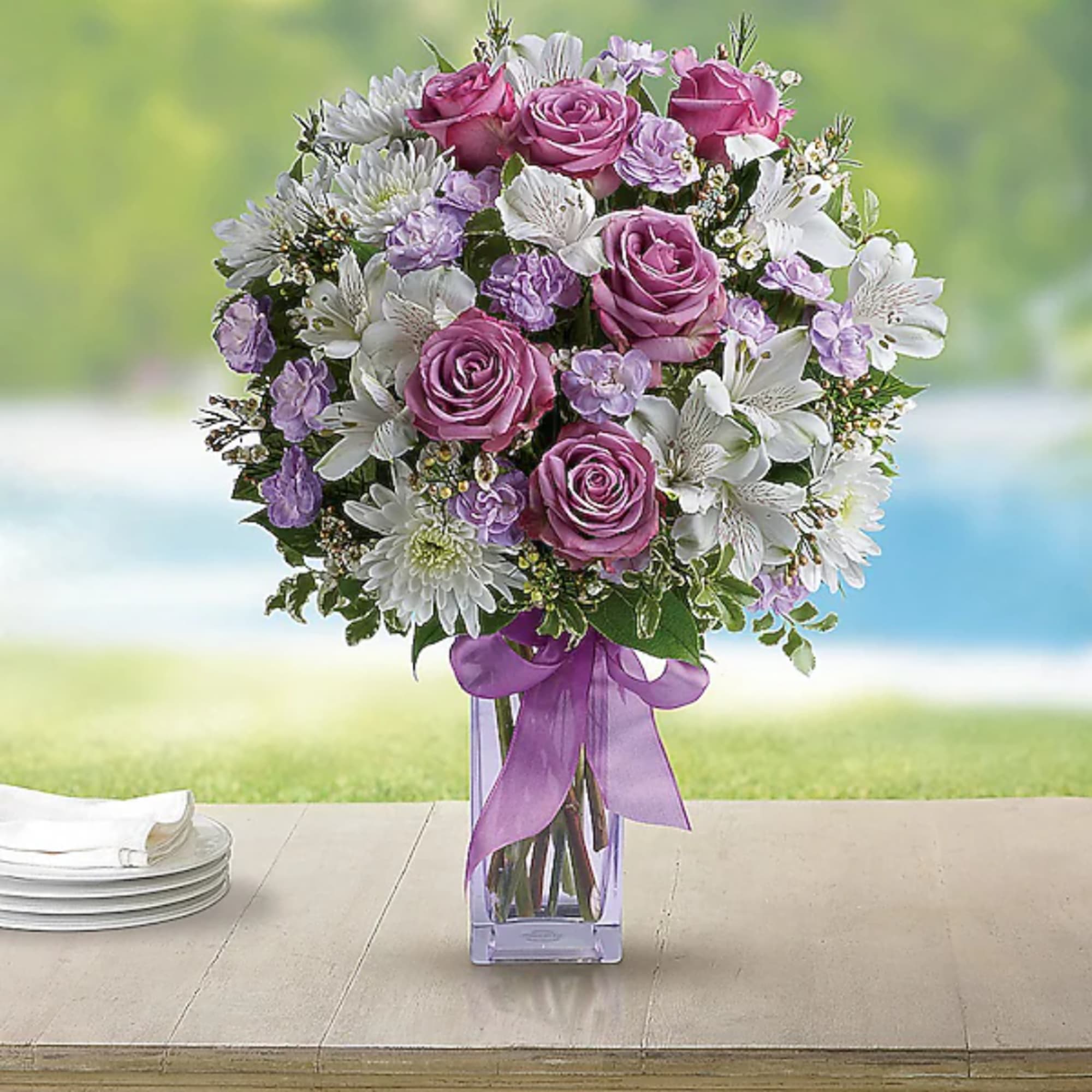 Pink roses and white flowers in a clear vase with a purple ribbon