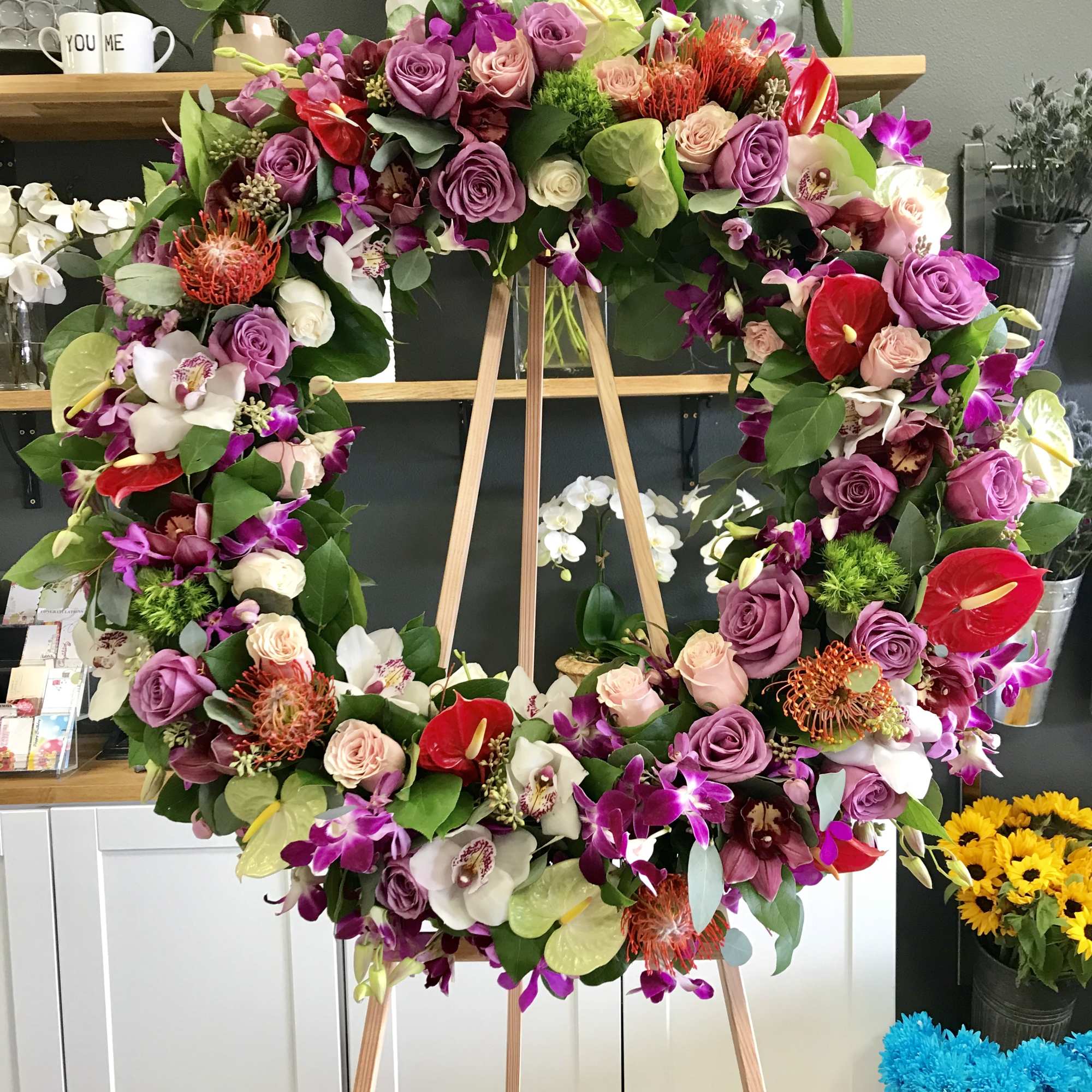 Large floral wreath on a wooden easel with purple, pink, white, and red blooms
