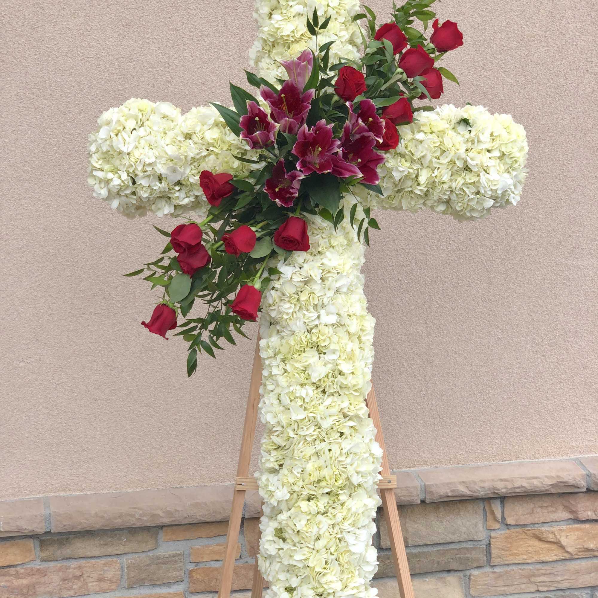 Floral cross on an easel with white blooms and red roses