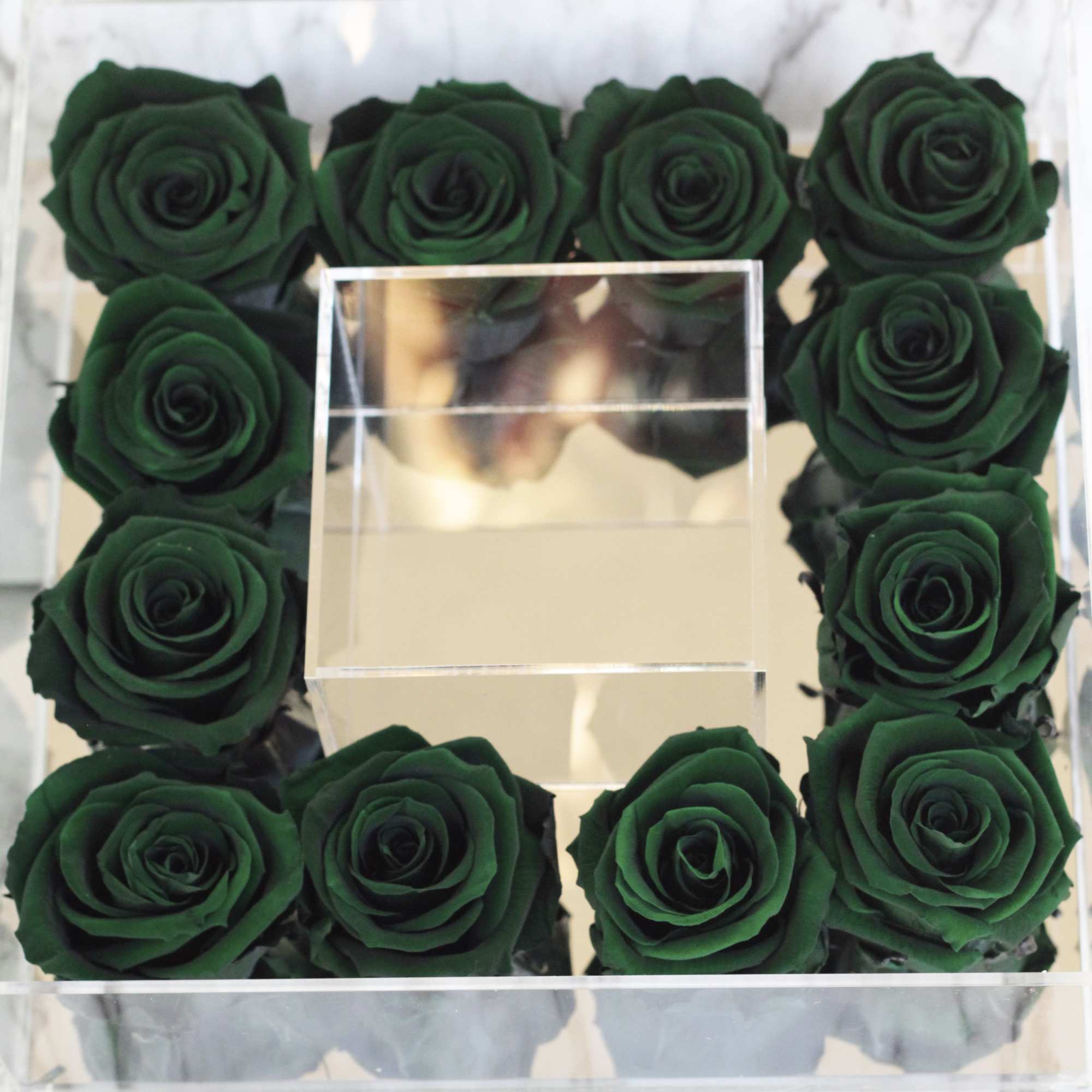 Square clear box filled with dark green roses around a mirrored center