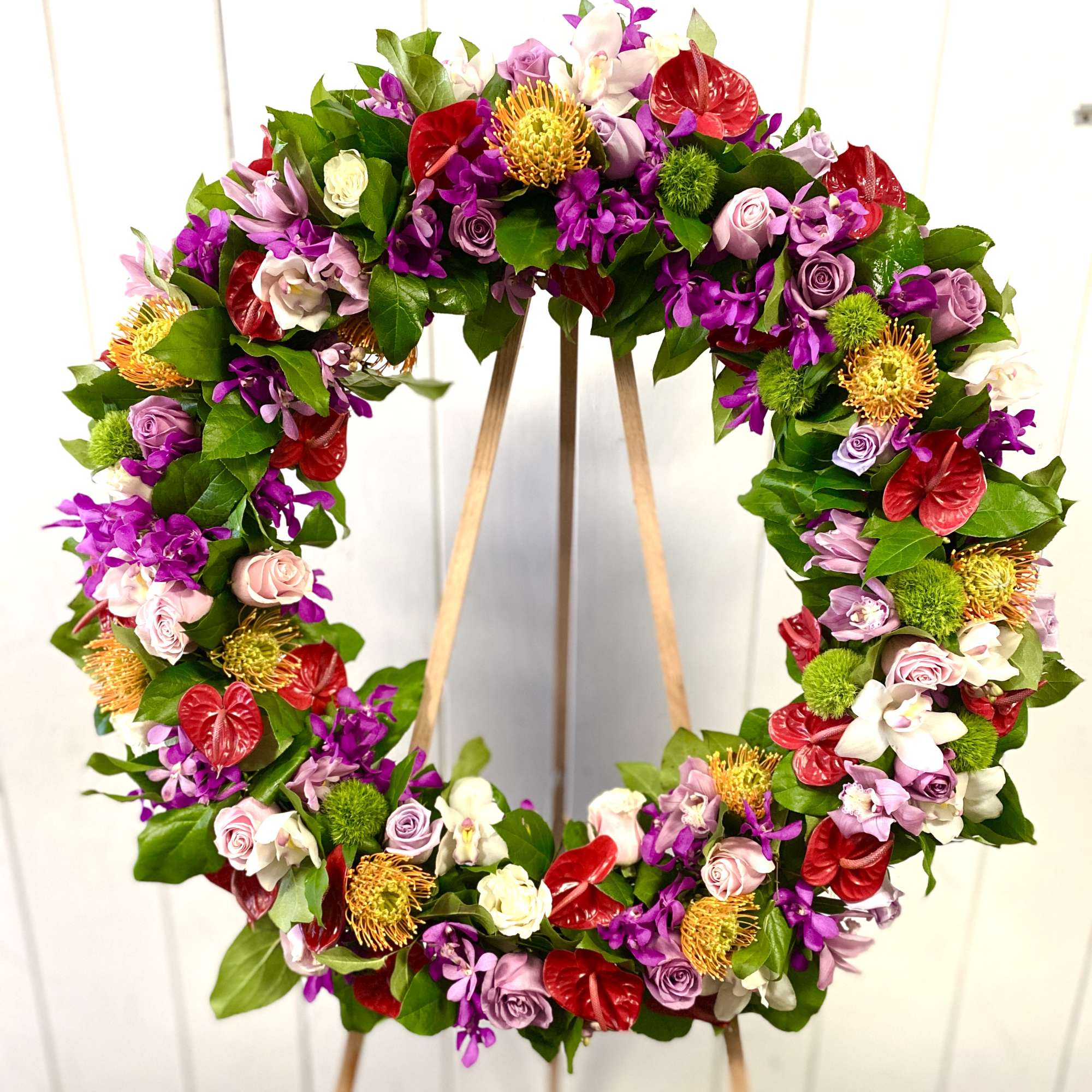 Circular floral wreath with purple, pink, red, and white blooms on a stand