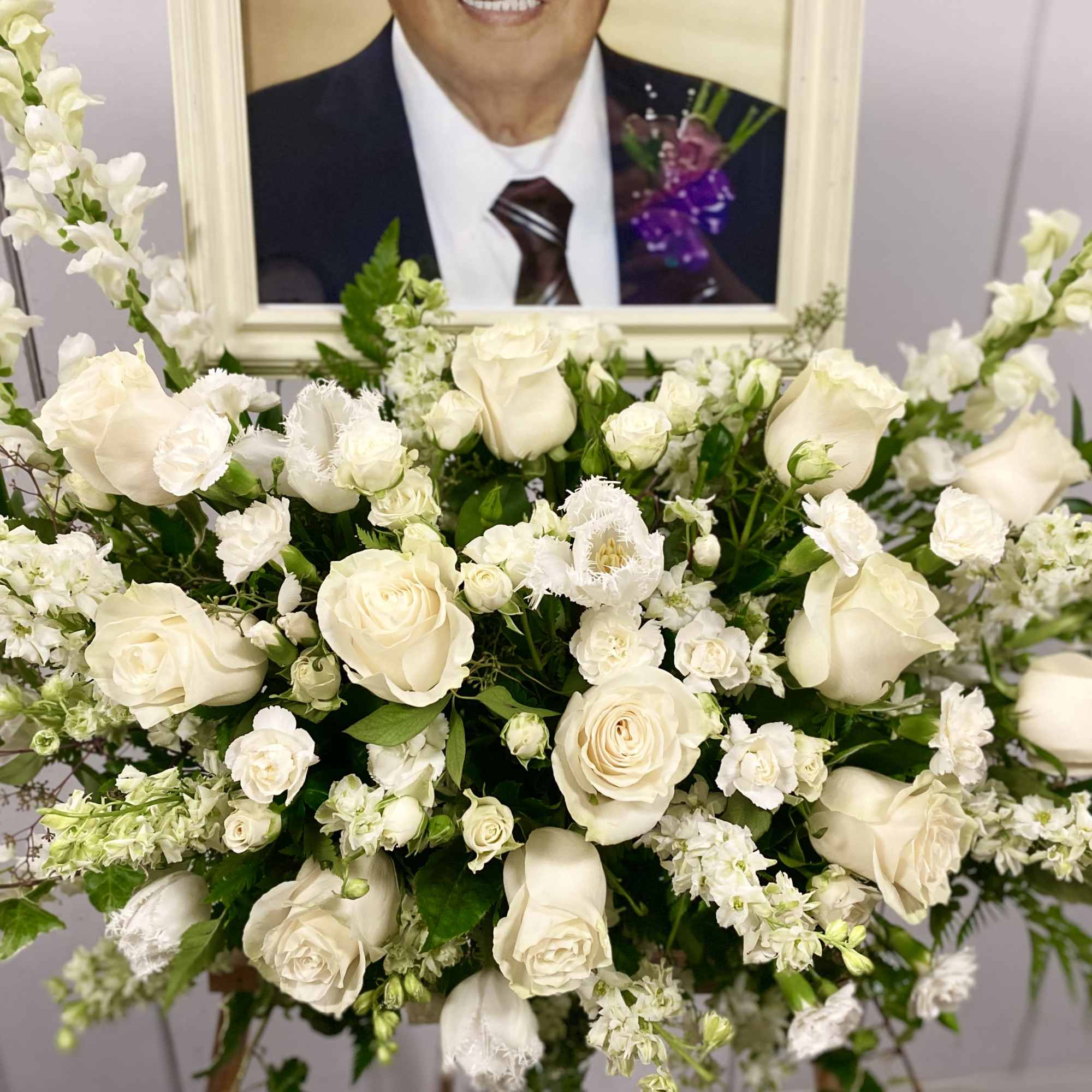 White rose and snapdragon arrangement in front of a framed portrait