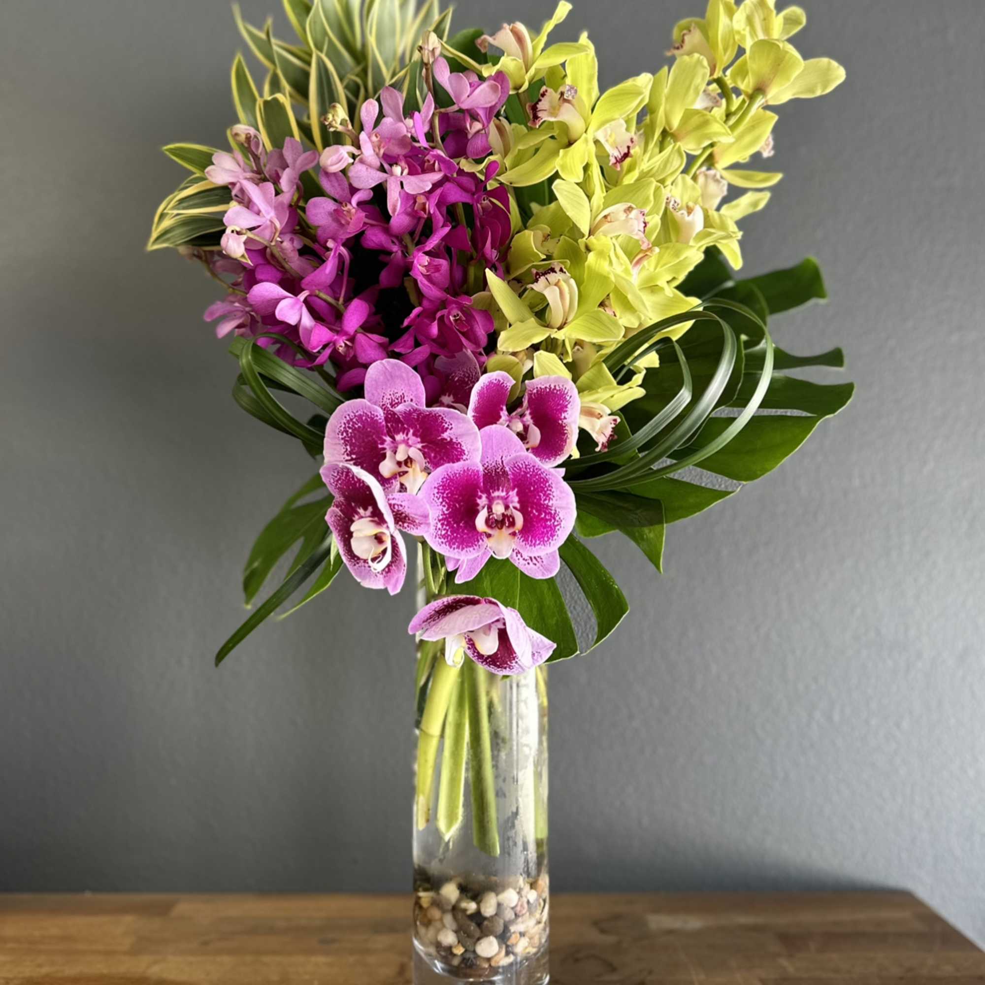 Pink and yellow orchids arranged in a tall glass vase.