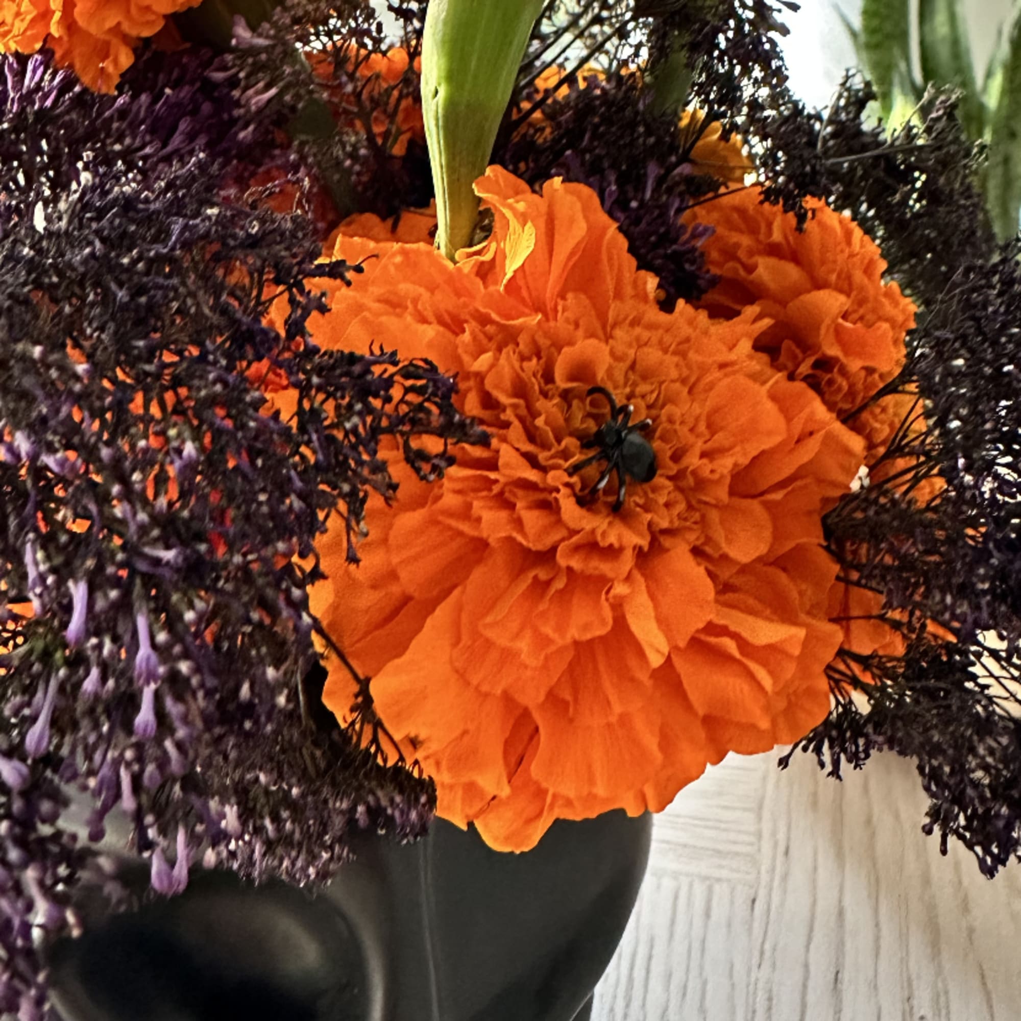 Orange marigolds with dark purple filler in a black vase