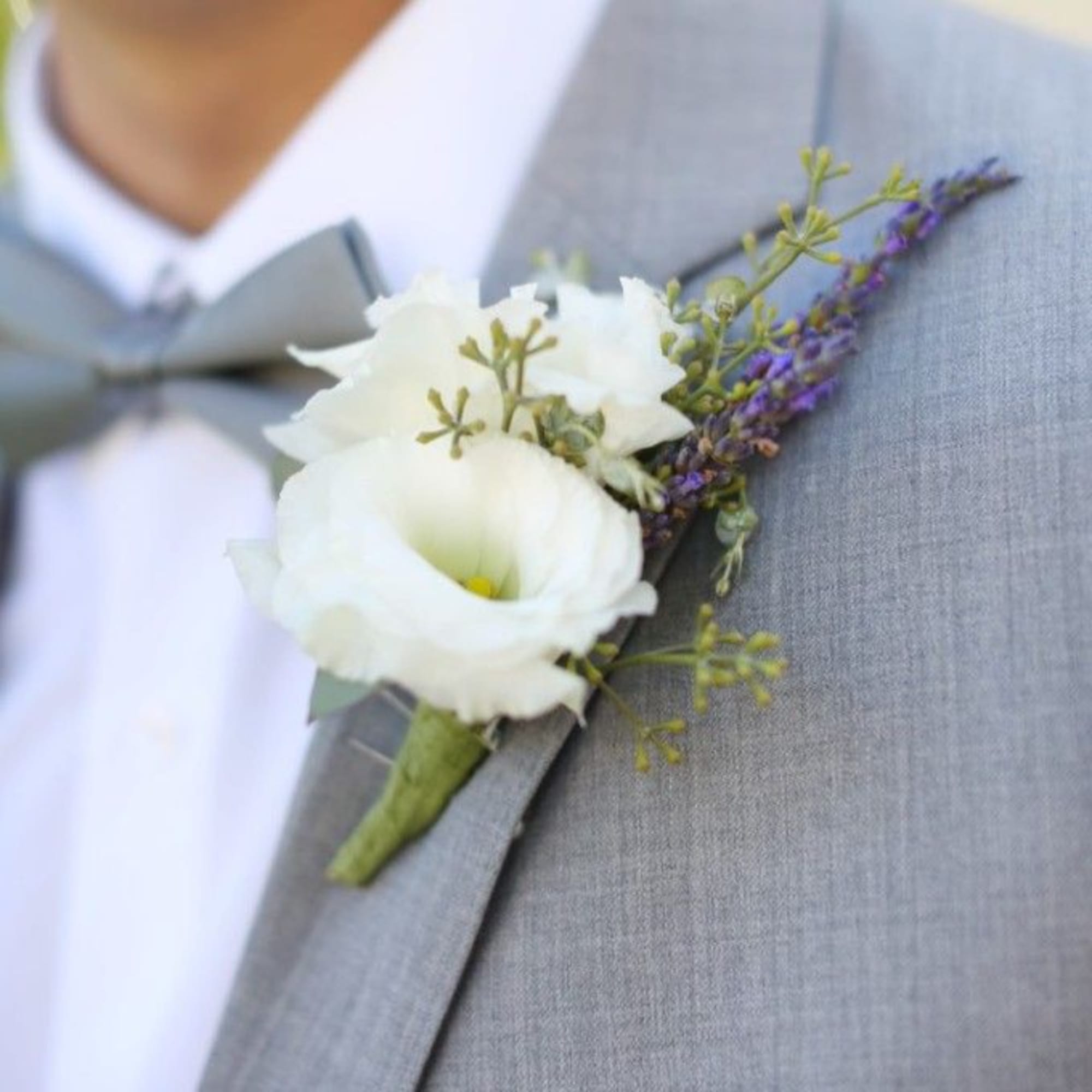 White boutonniere with purple accents pinned to a gray suit jacket