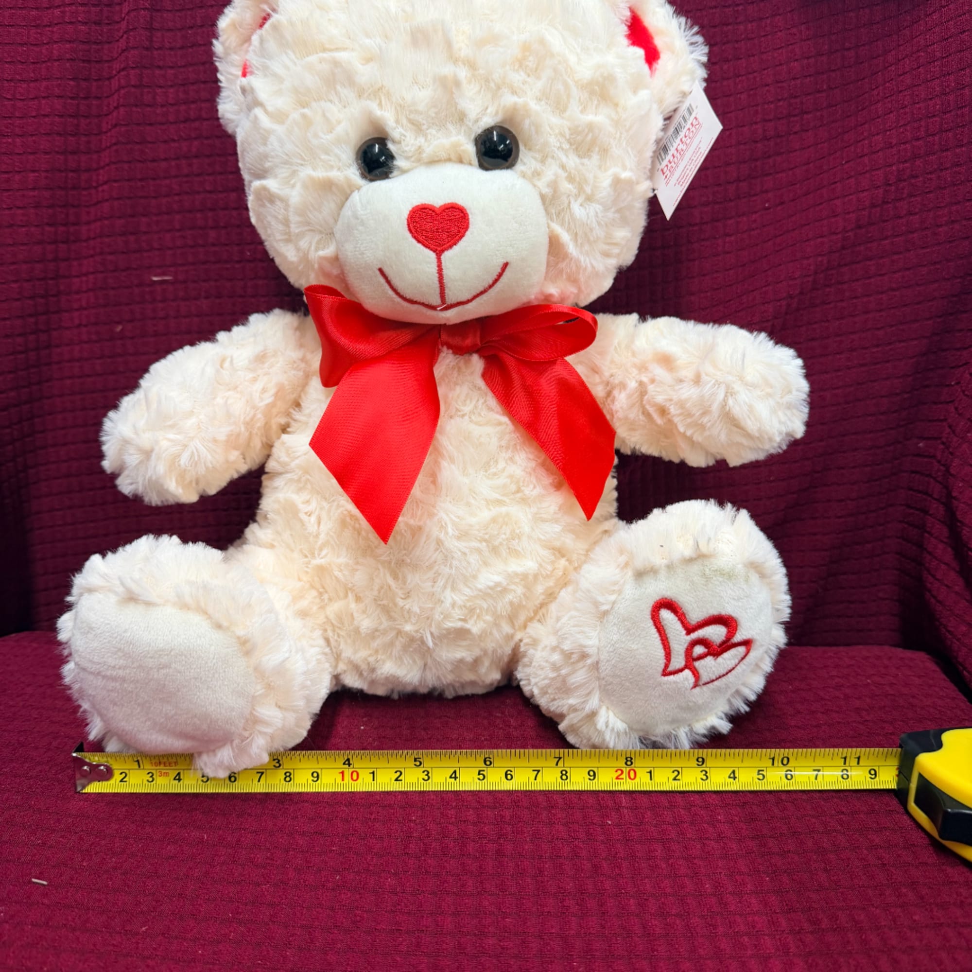 Cream teddy bear with a red bow sitting on a purple fabric background