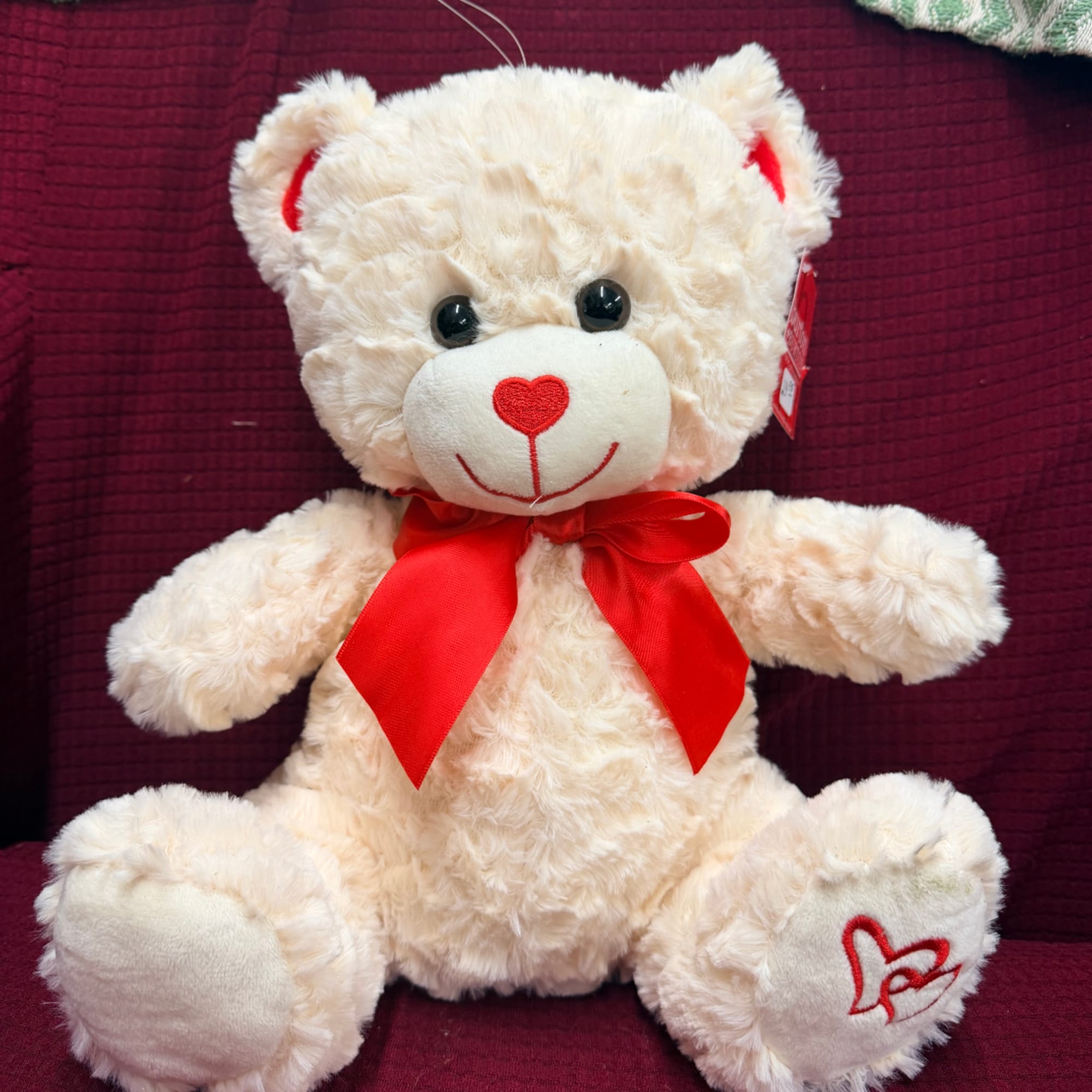 Cream teddy bear with a red bow sitting on a burgundy chair, photo 2 of 4