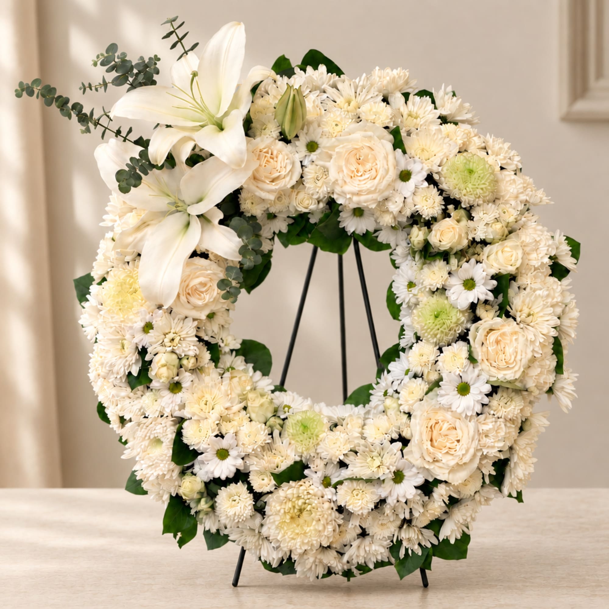 White floral wreath with lilies, roses, and daisies on a stand