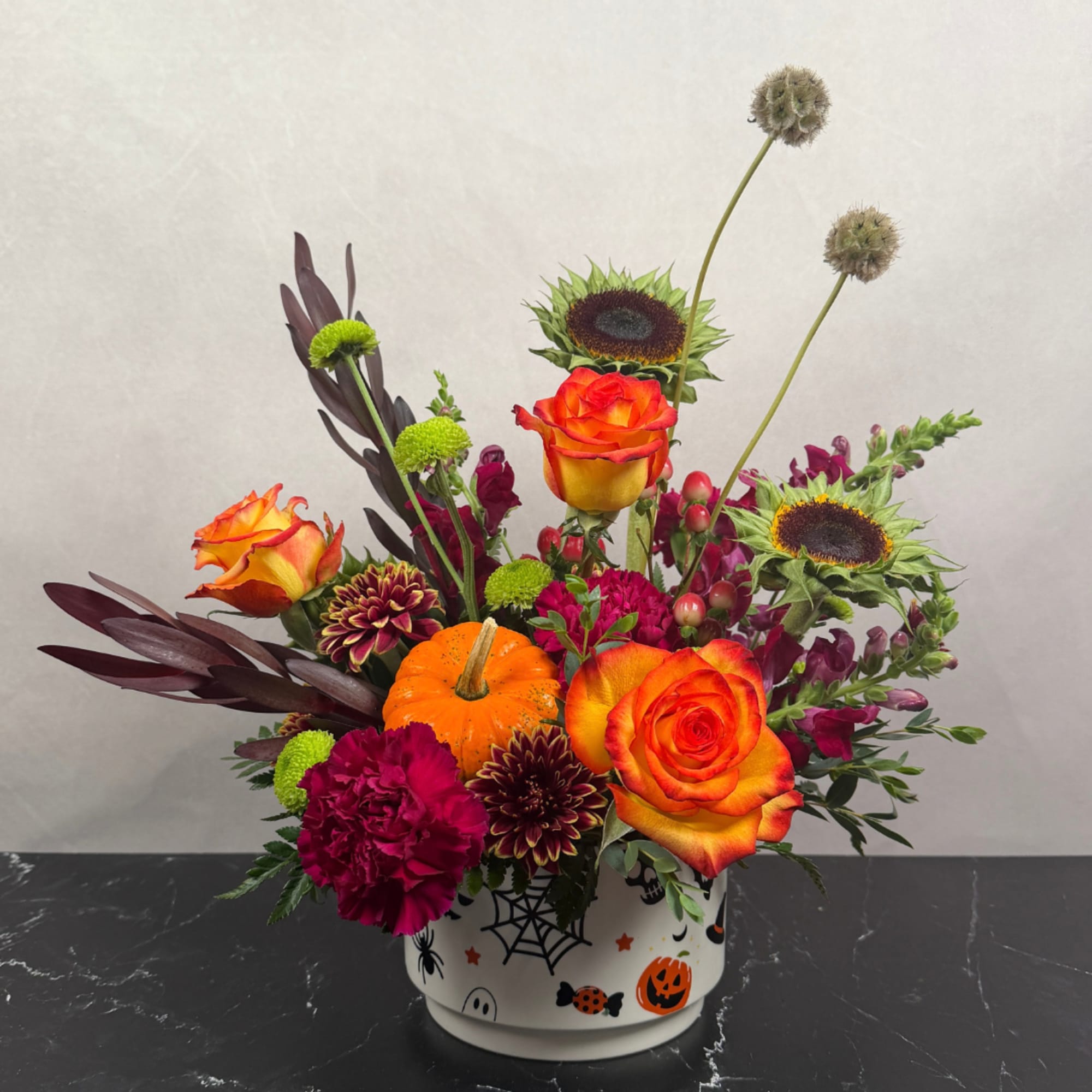 Halloween floral arrangement in a decorated ceramic pot with orange roses and sunflowers