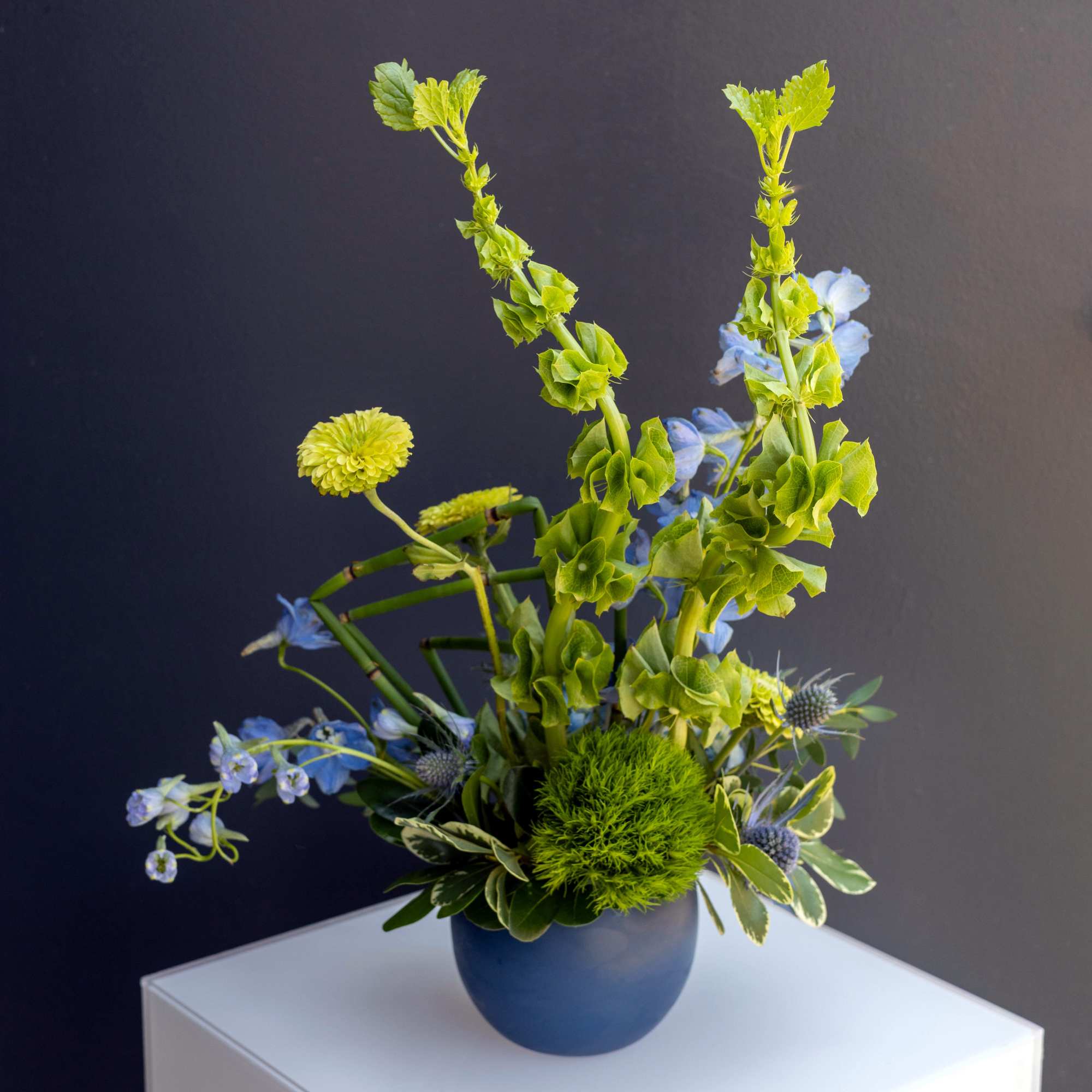 Blue and green floral arrangement in a round vase