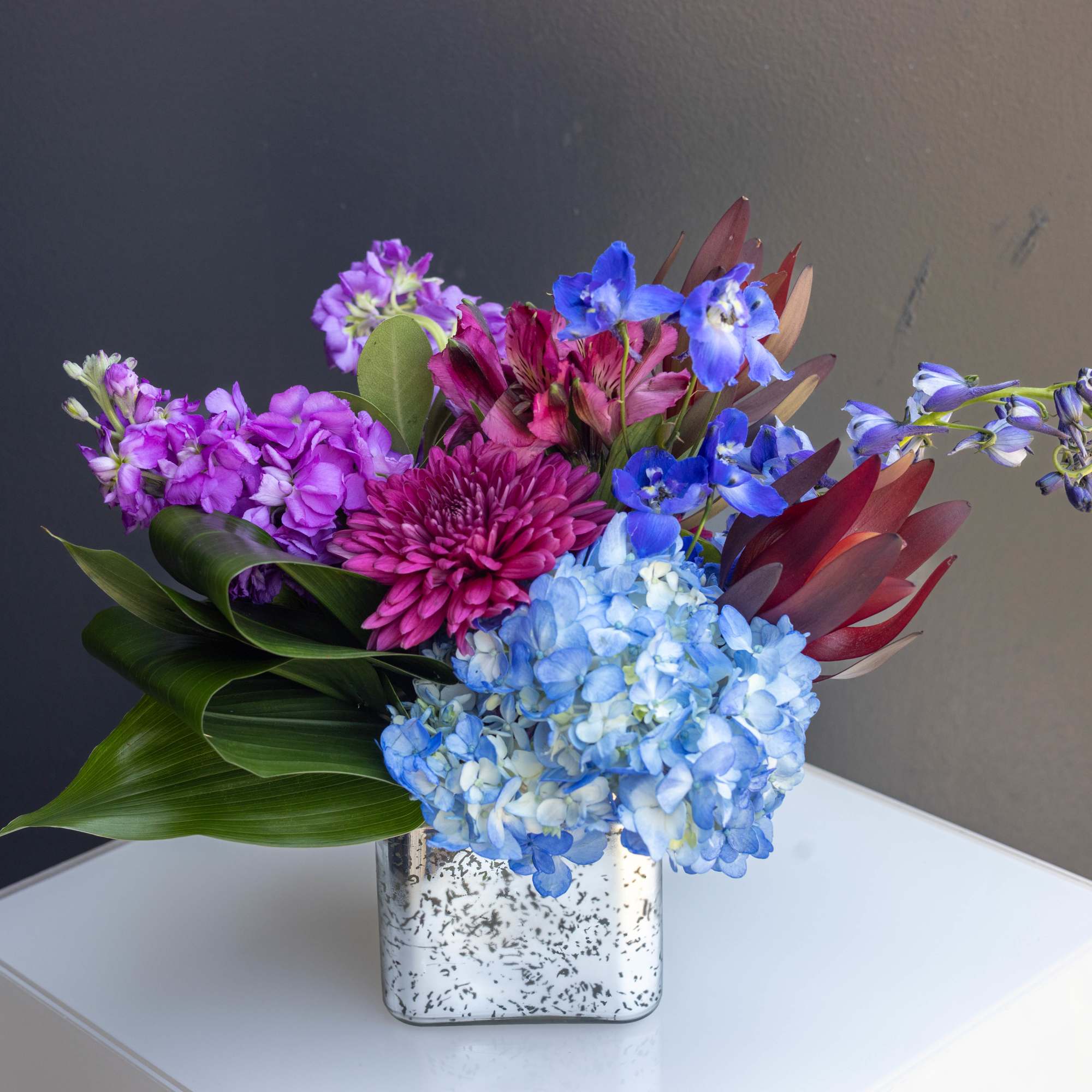 Colorful bouquet in a speckled square vase with blue hydrangea and purple blooms