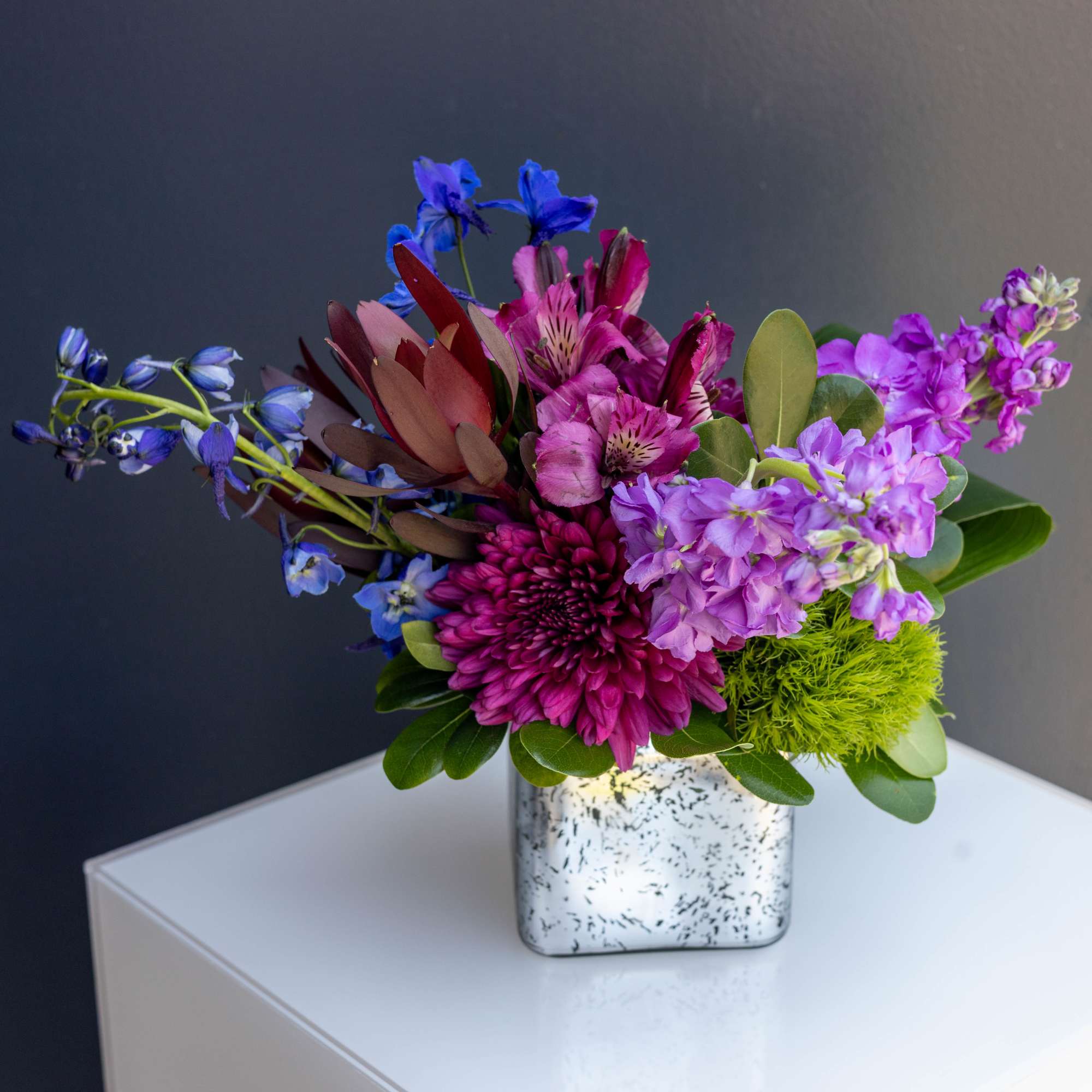Colorful bouquet in a speckled square vase with purple and blue flowers