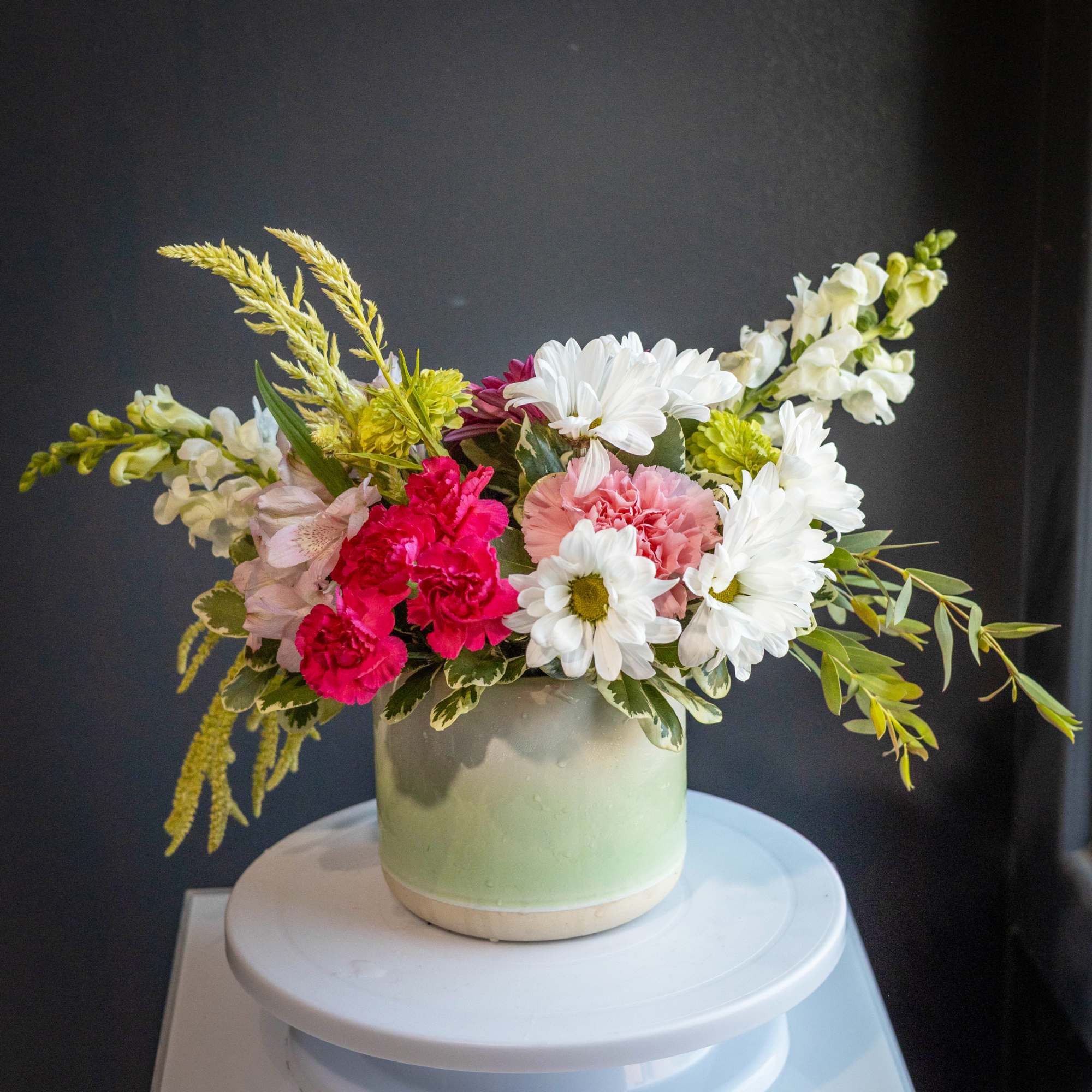 Mixed bouquet of pink, white, and yellow flowers in a pale green vase