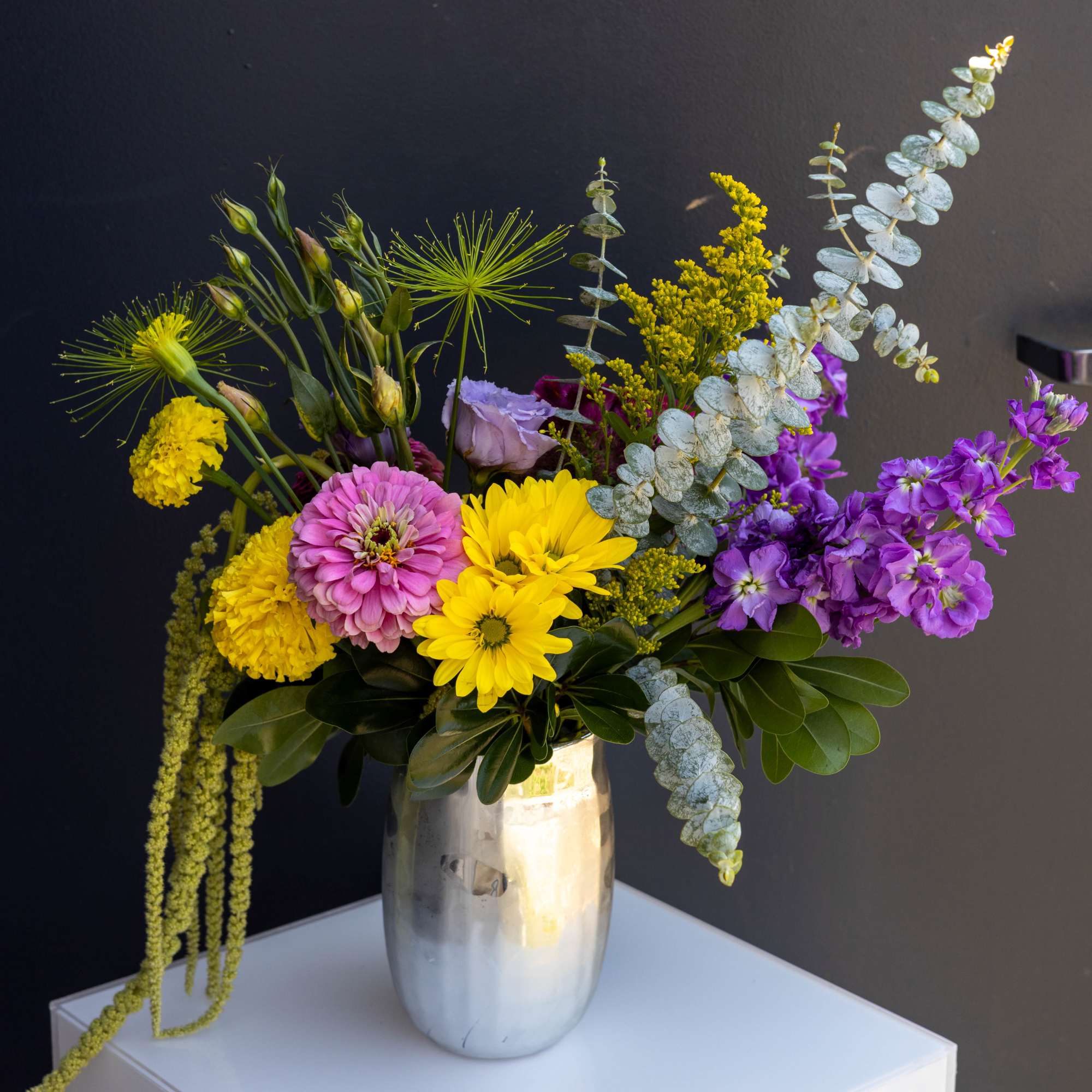 Mixed bouquet of yellow, pink, and purple flowers in a silver vase