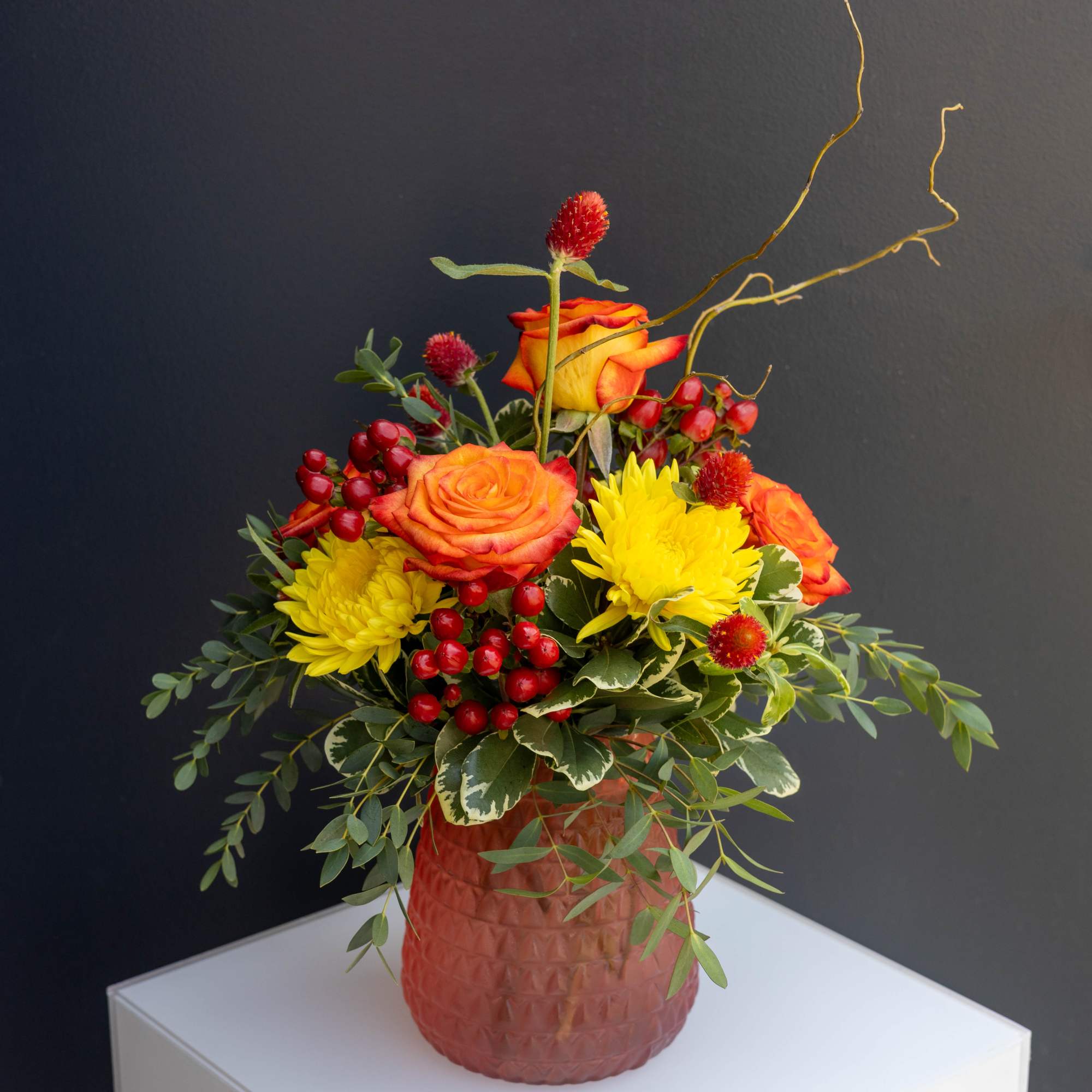 Orange roses and yellow chrysanthemums in a textured vase with red berries